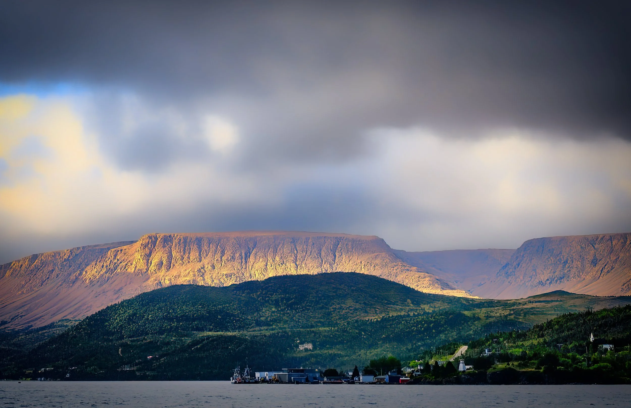 The Tablelands dramatically lit up in the light of the rising sun through storm clouds near Woody Point, Newfoundland. The tablelands are a rare, rust-colored landscape formed by exposed rock from the Earth's mantle.  