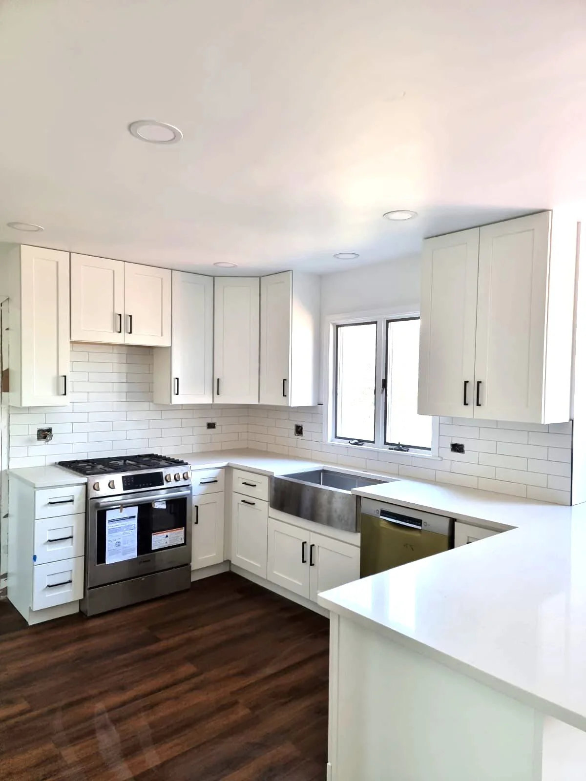 Empty modern kitchen with white cabinets, stainless steel appliances, and dark wood flooring.