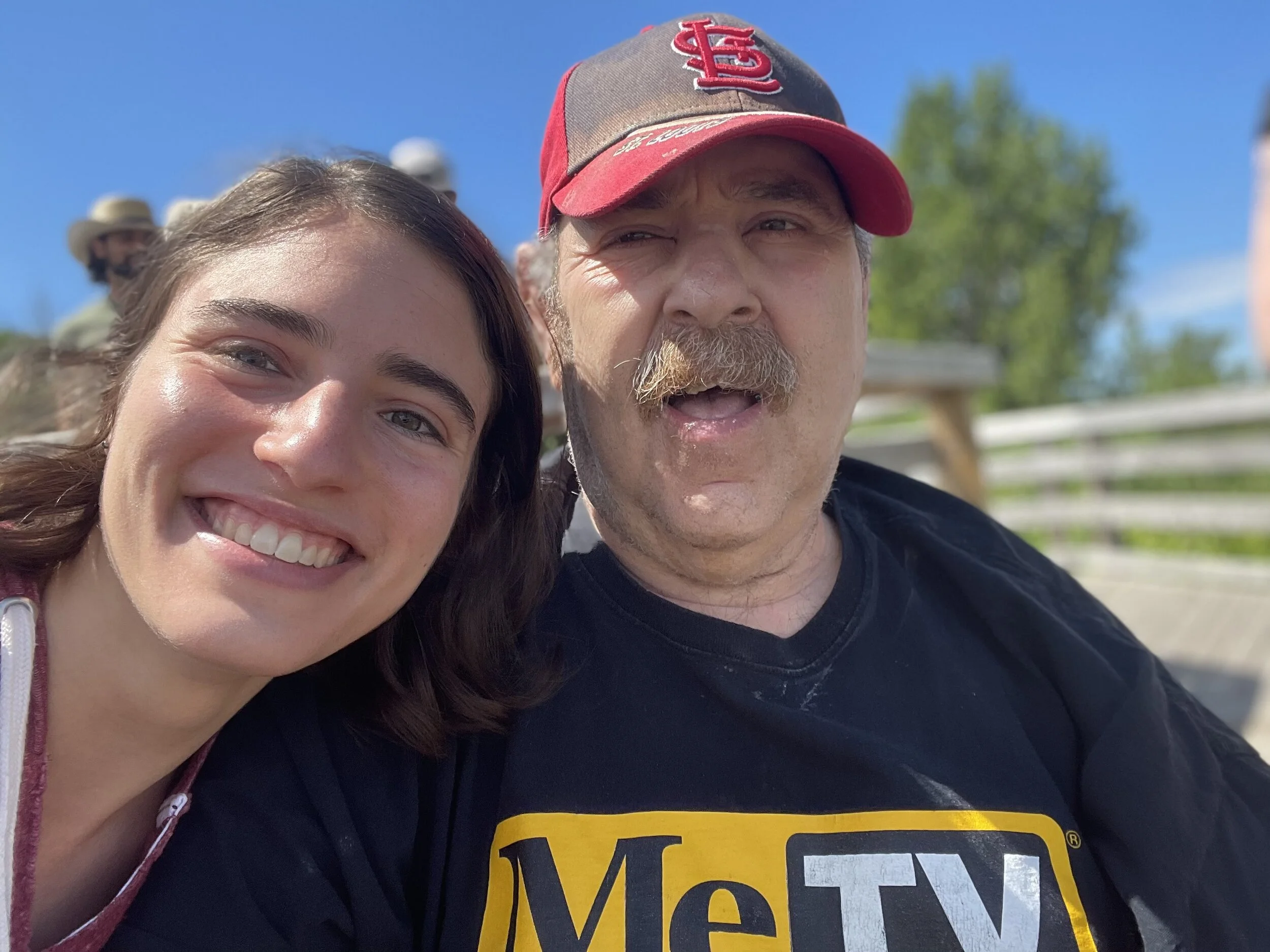 Close up of two people leaning into each other, smiling at the camera, with blue sky behind them.