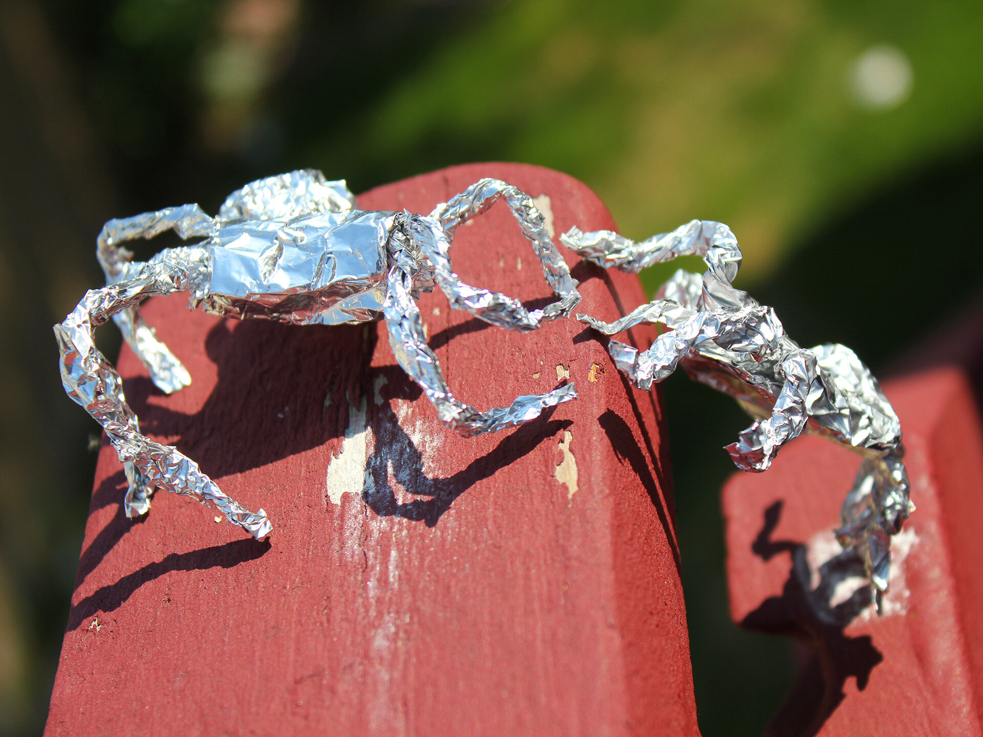 Two Tin Foil Spiders Climbing Railing