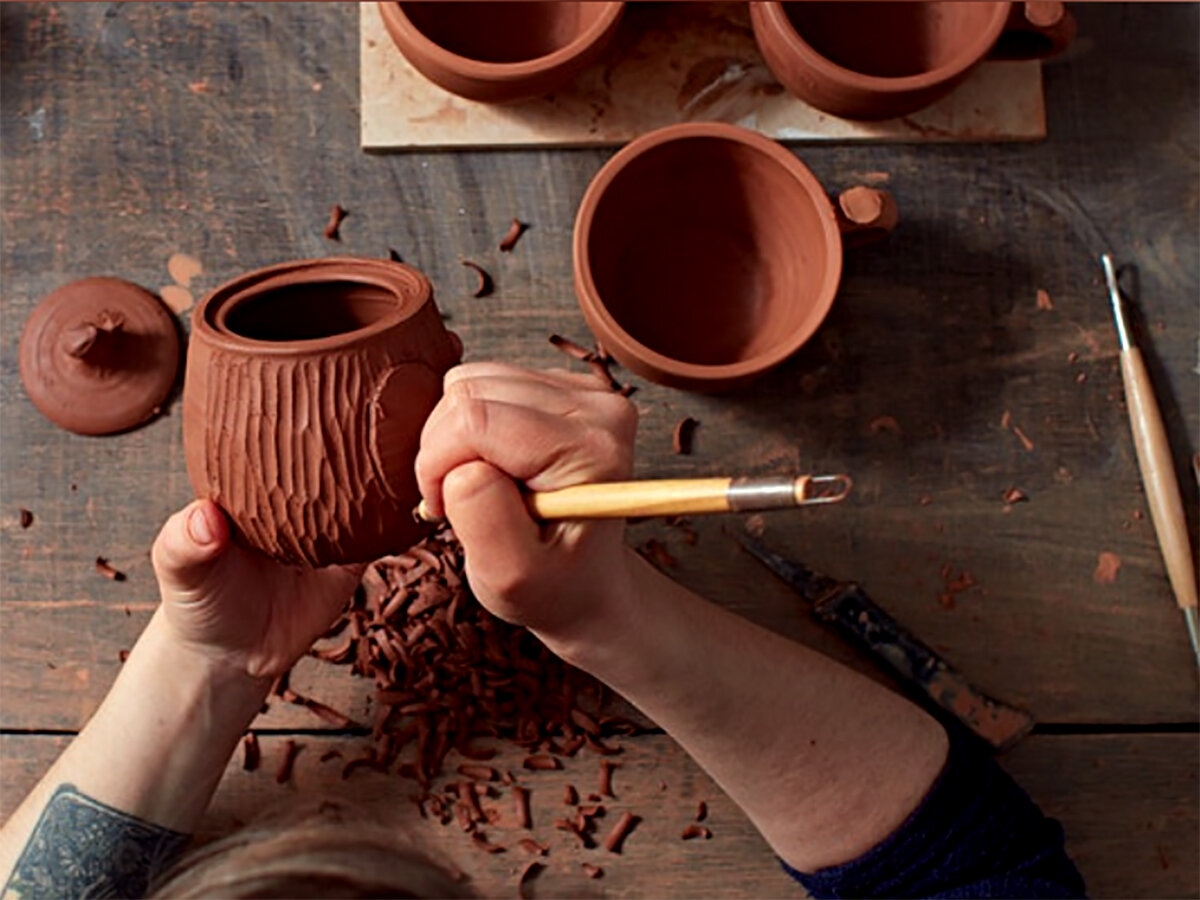 Artist adding elaborate carvings to terracotta pot