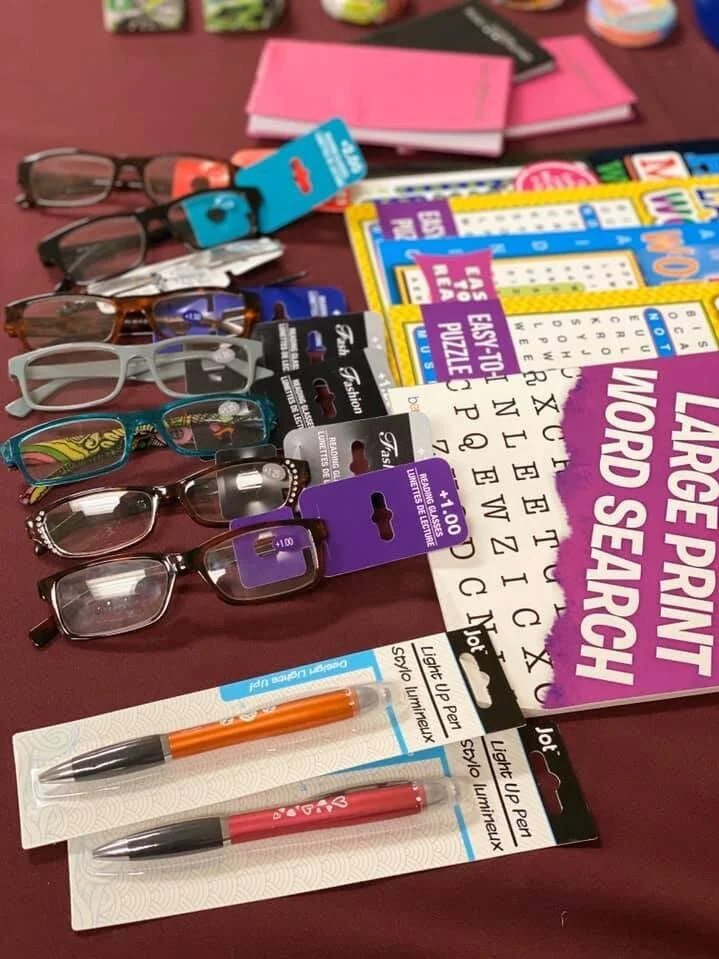 A collection of eyeglasses, pens, word search, bingo cards, and a large print book on a table.