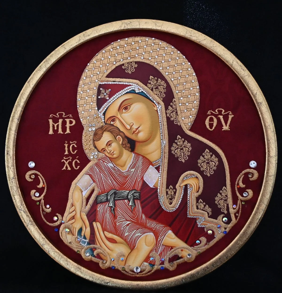 #EMB12 PANAGIA KYKKOTISSA  $235
DESCRIPTION:  Embroidered icon (10 ½”x 13 ½”) is matted to round gilded metal gold frame (14” x 17”) on a burgundy damask background. Panagia’s garments are richly highlighted with burgundy satin, over which rich desig