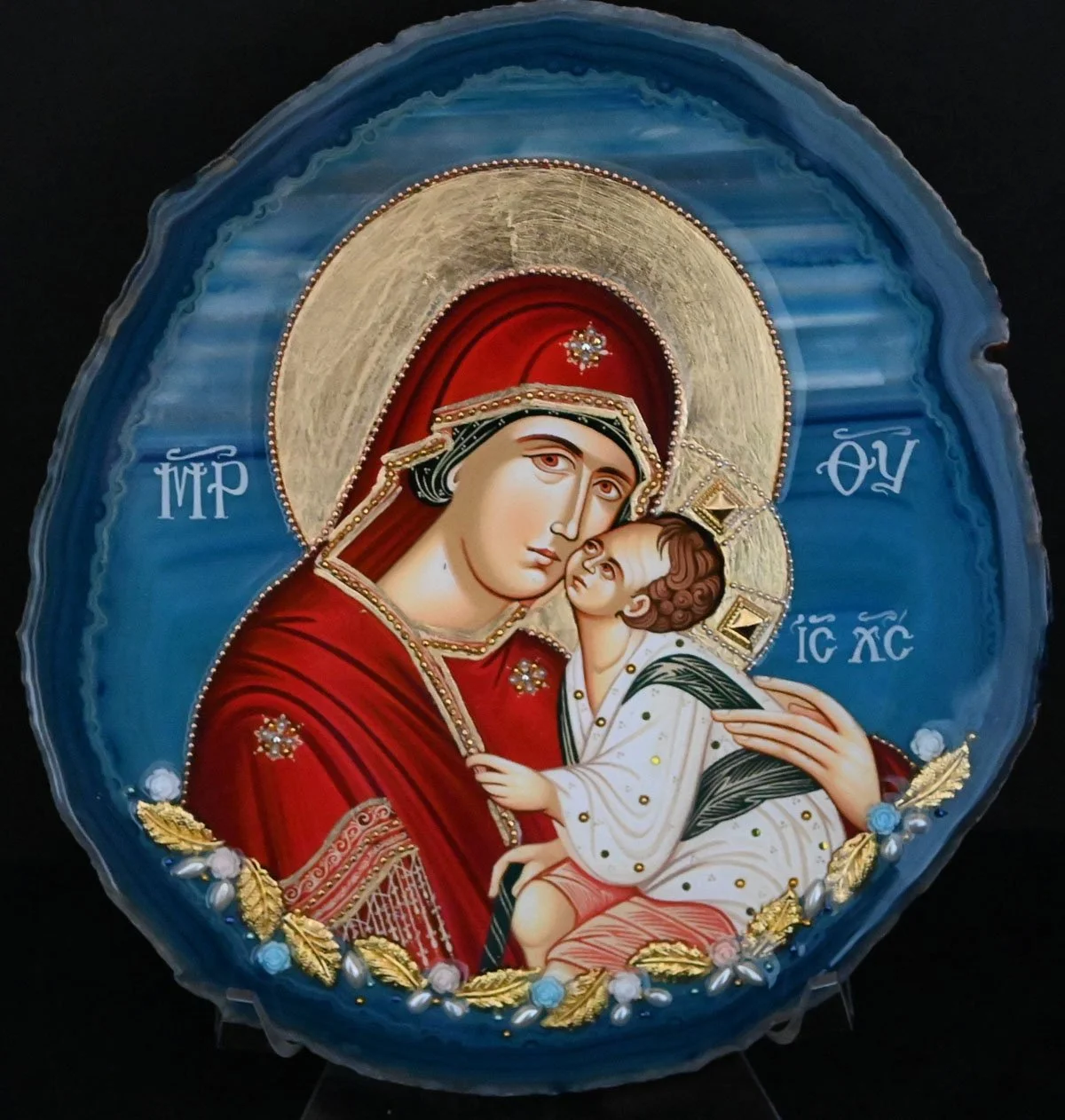 #AG10 PANAGIA NISIOTISSA  $140   
DESCRIPTION: The icon is mounted on a blue-edged Brazilian agate slice with light blue and white striping.  (8 x 7 ½ x ¼ ) 1.2 lbs. The photostephano (halo) is hand-gilded gold, encircled with a rose gold metal stran