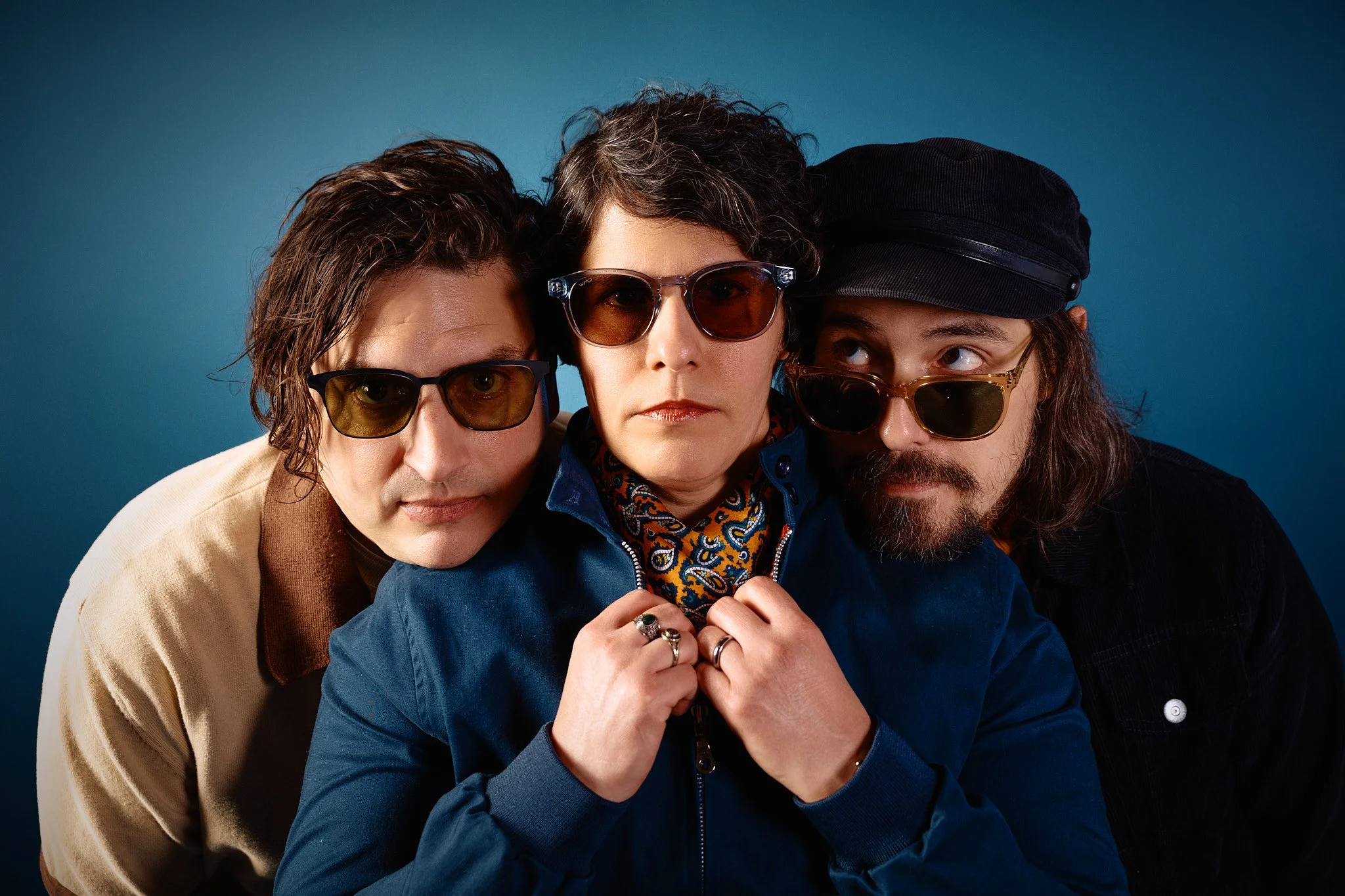 Three people close together wearing sunglasses against a blue background.