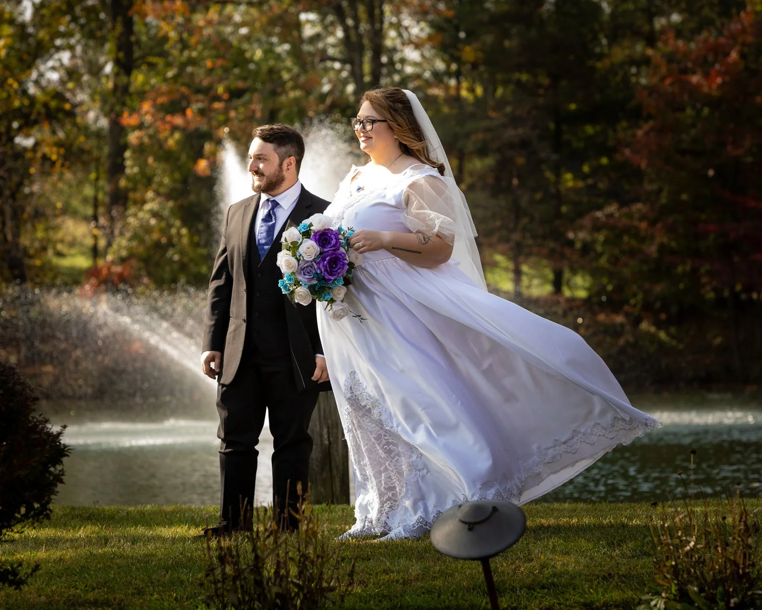 Fall wedding couple by a fountain with dress blowing