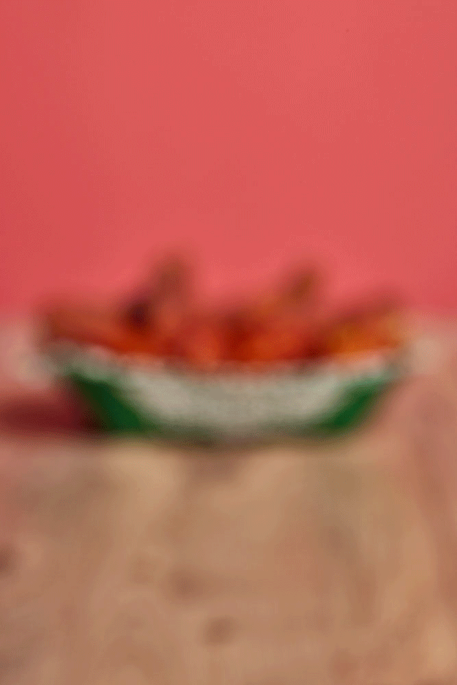 Blurred image of a green and white fruit bowl with watermelon slices, pink background