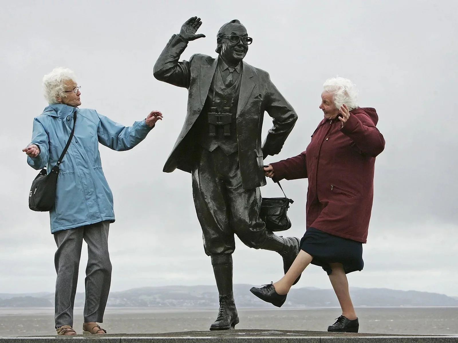 two older women happily dancing around a statue