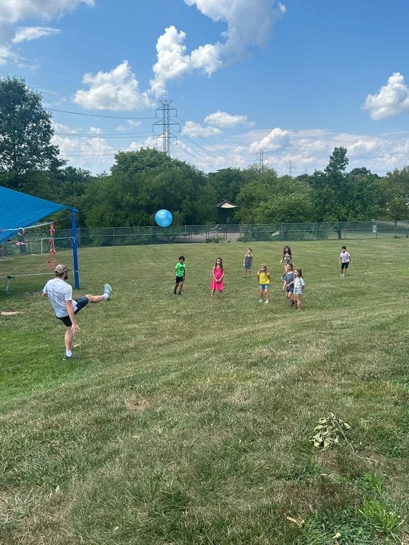 Children playing with a blue ball outdoors on a grassy field.