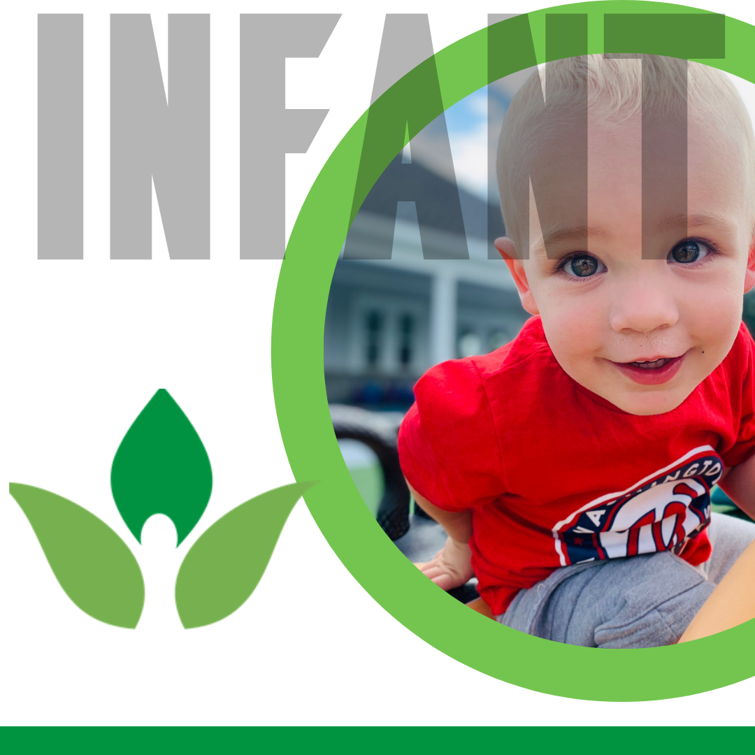 A young boy with blonde hair and wearing a red shirt smiling outdoors, with a house and mountain in the background.