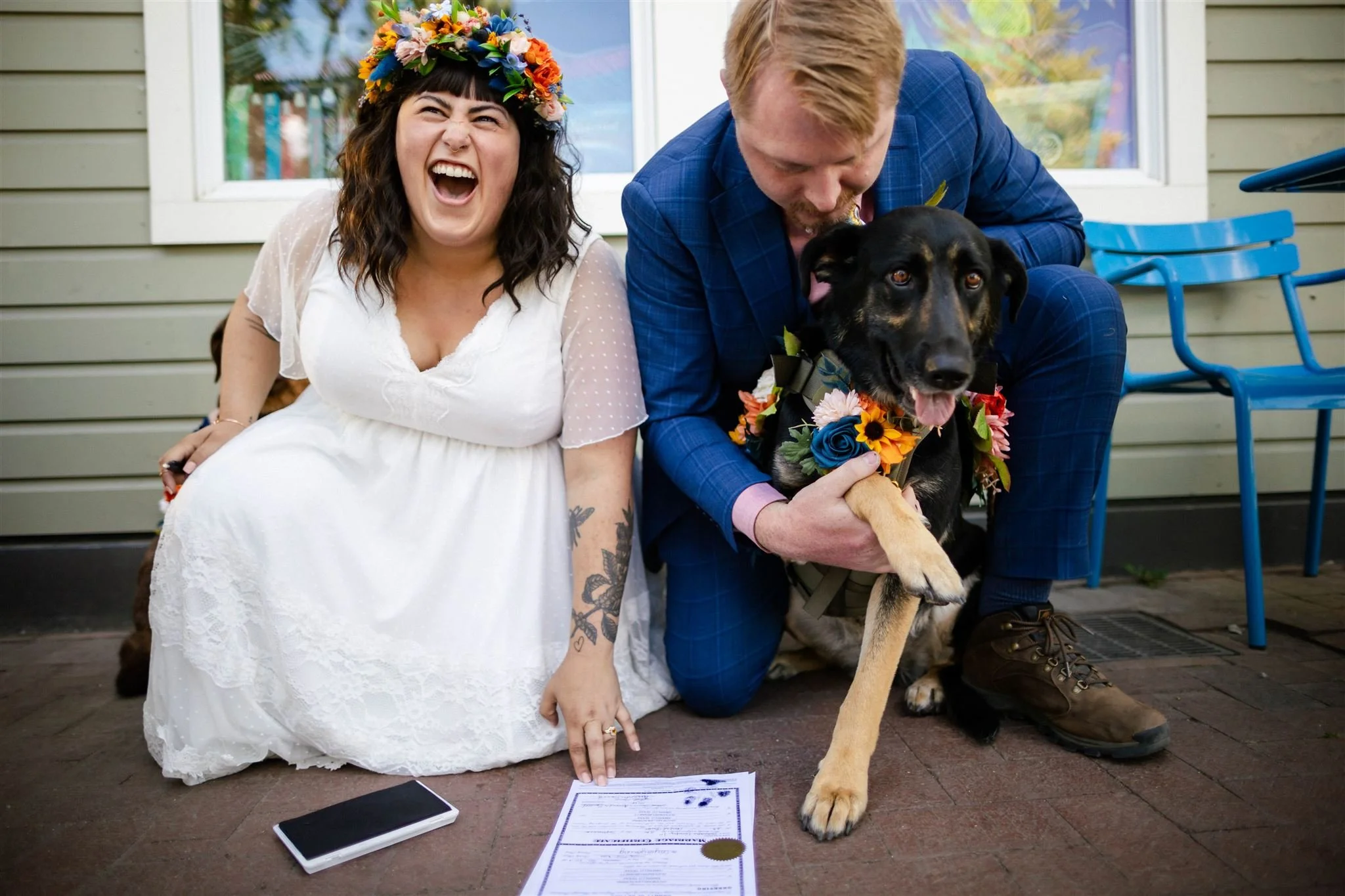 Bride laughs as groom helps their dog to sign their marriage license