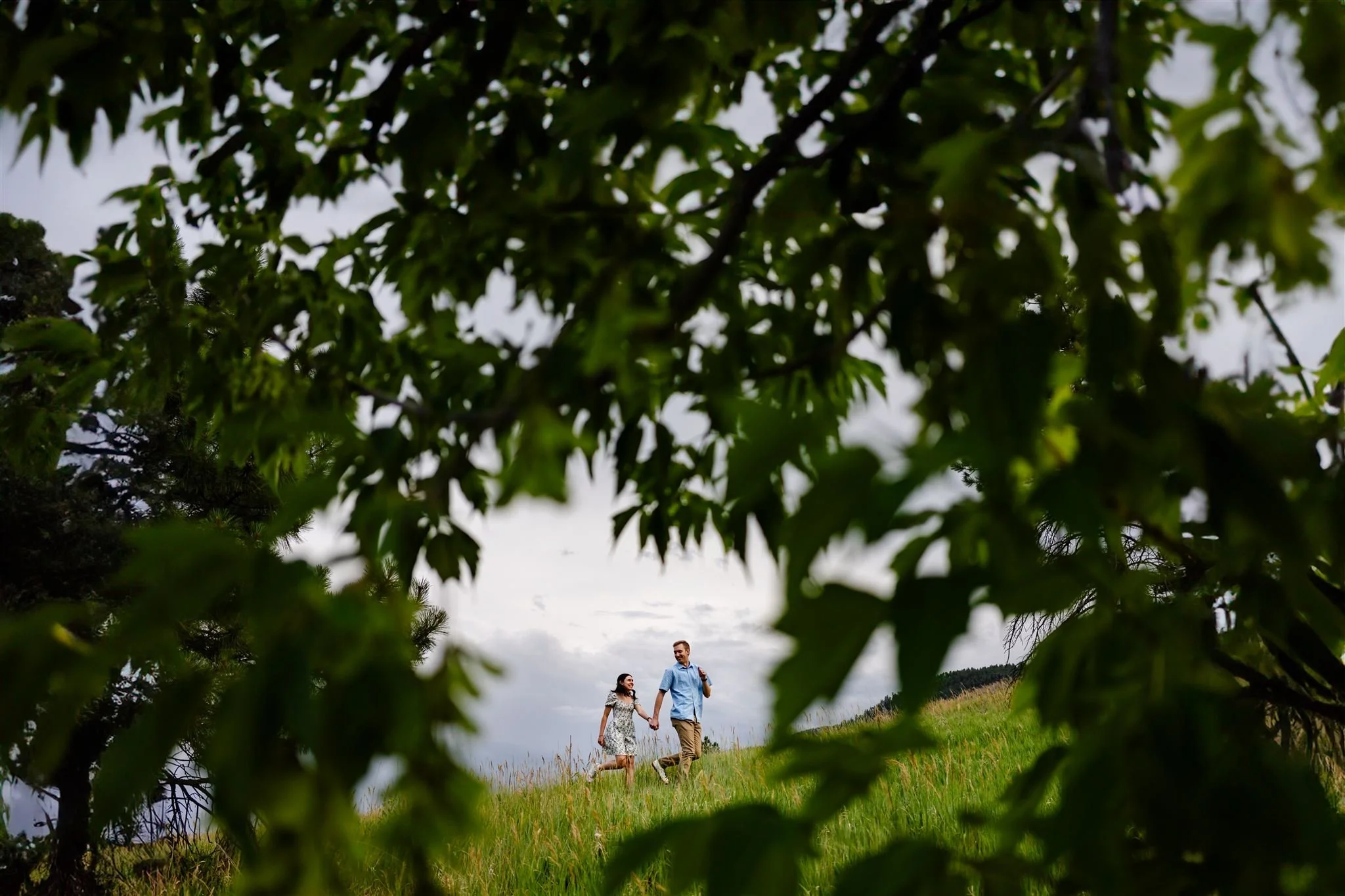 Couple running in field framed by tree