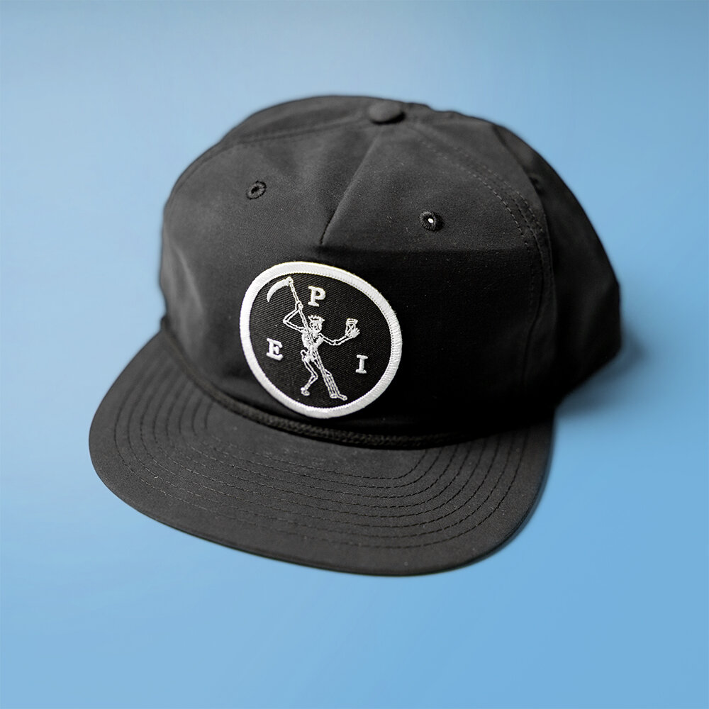 Black baseball cap with a white embroidered patch of a skeleton holding a golf club, with the letters E, P, and I around it, on a blue background.