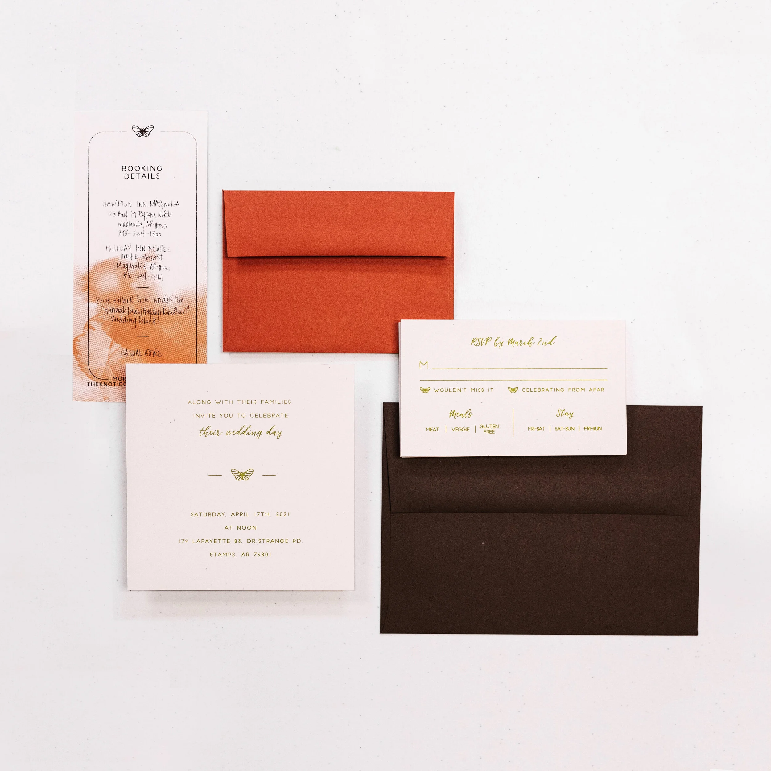 Wedding invitation set including an invitation card, RSVP card, red envelope, and a booking details card on a white surface.