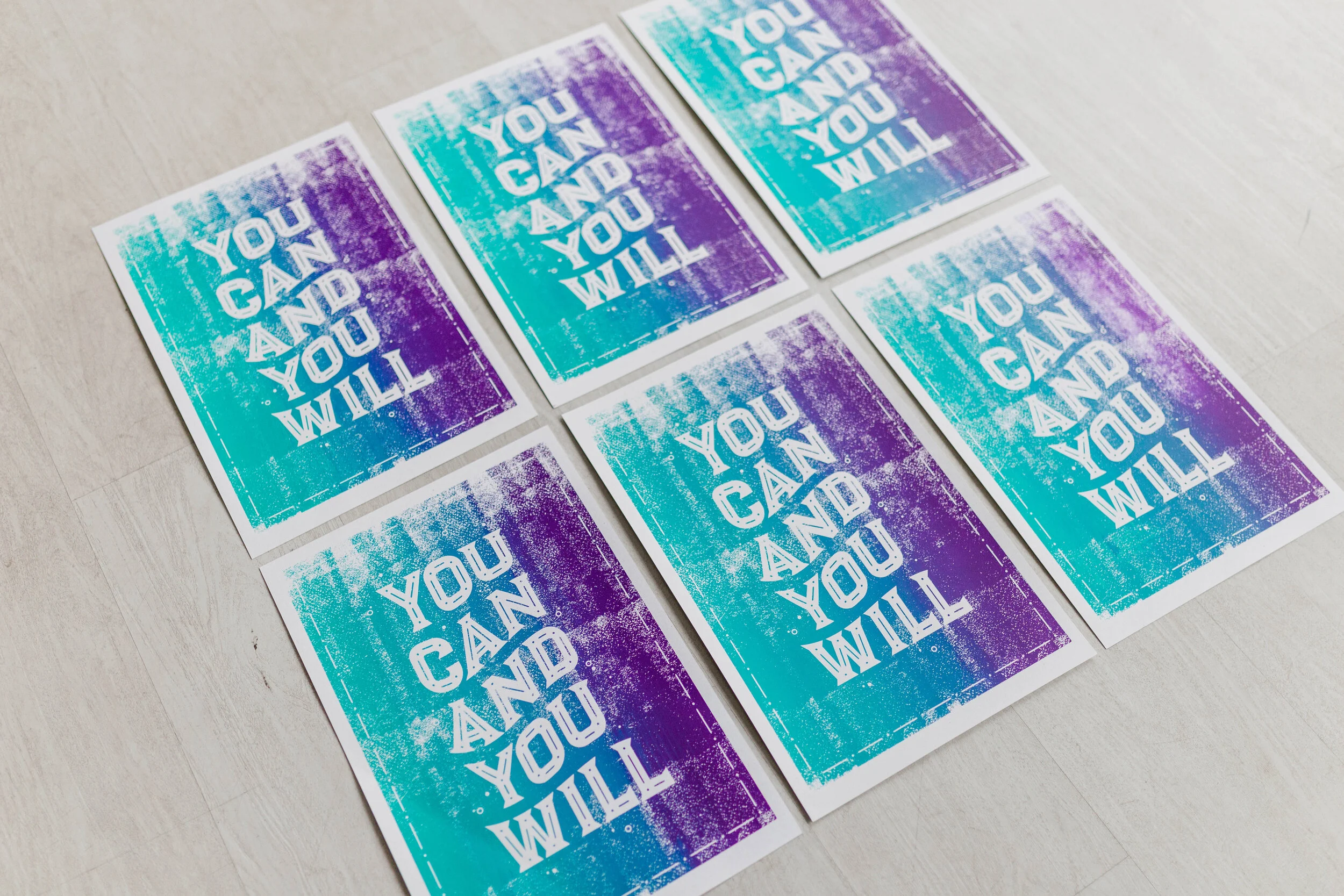 Six printed cards on a light-colored surface featuring a gradient background of blue and purple with the motivational phrase 'You can and you will' in bold white uppercase letters.