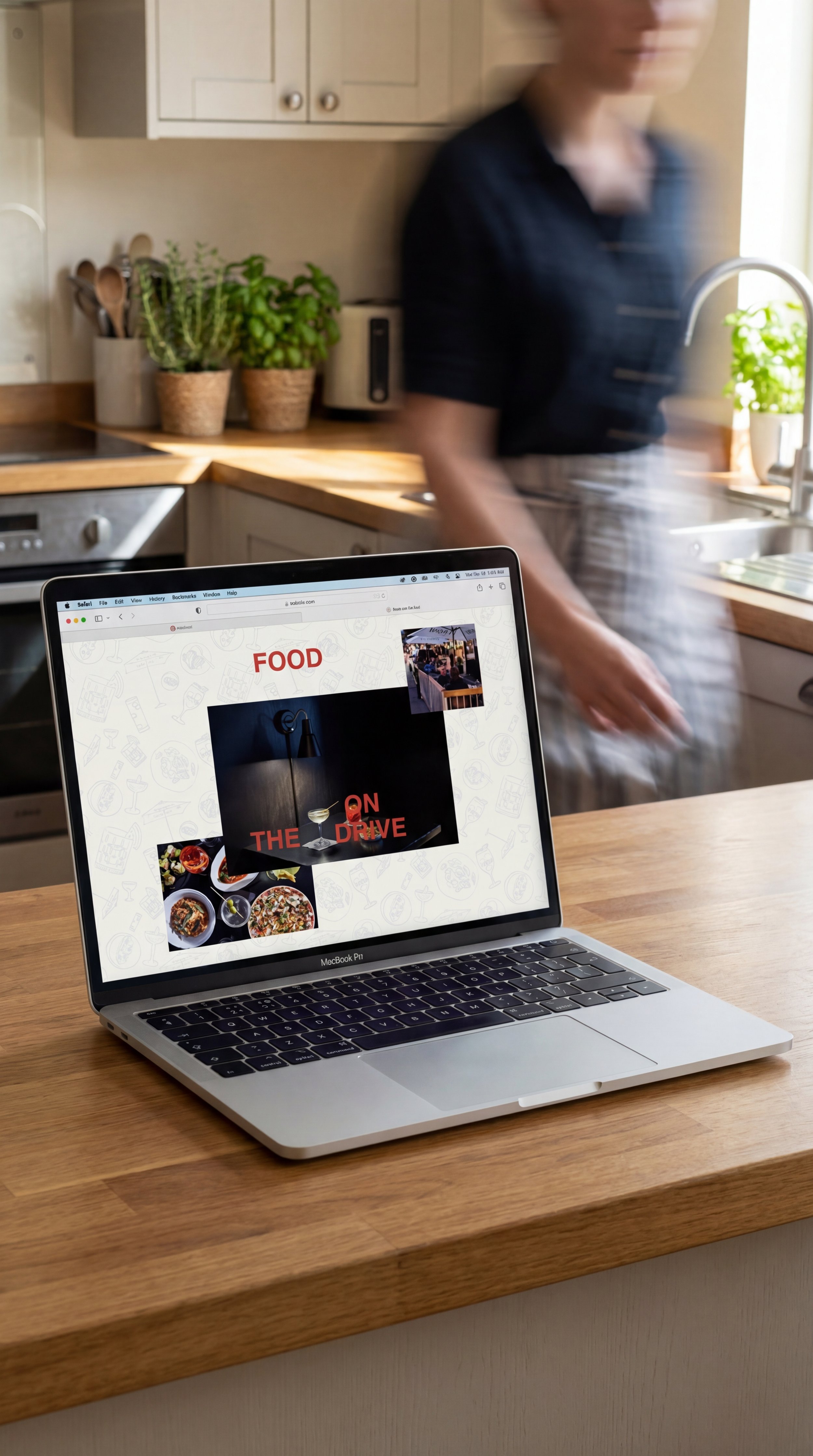 Open laptop on a wooden kitchen table displaying a website that's titled Bar Corso, with "Food on the drive" on screen plus images of food and a drink. A person moving in a kitchen background with potted plants, and a window with sunlight.