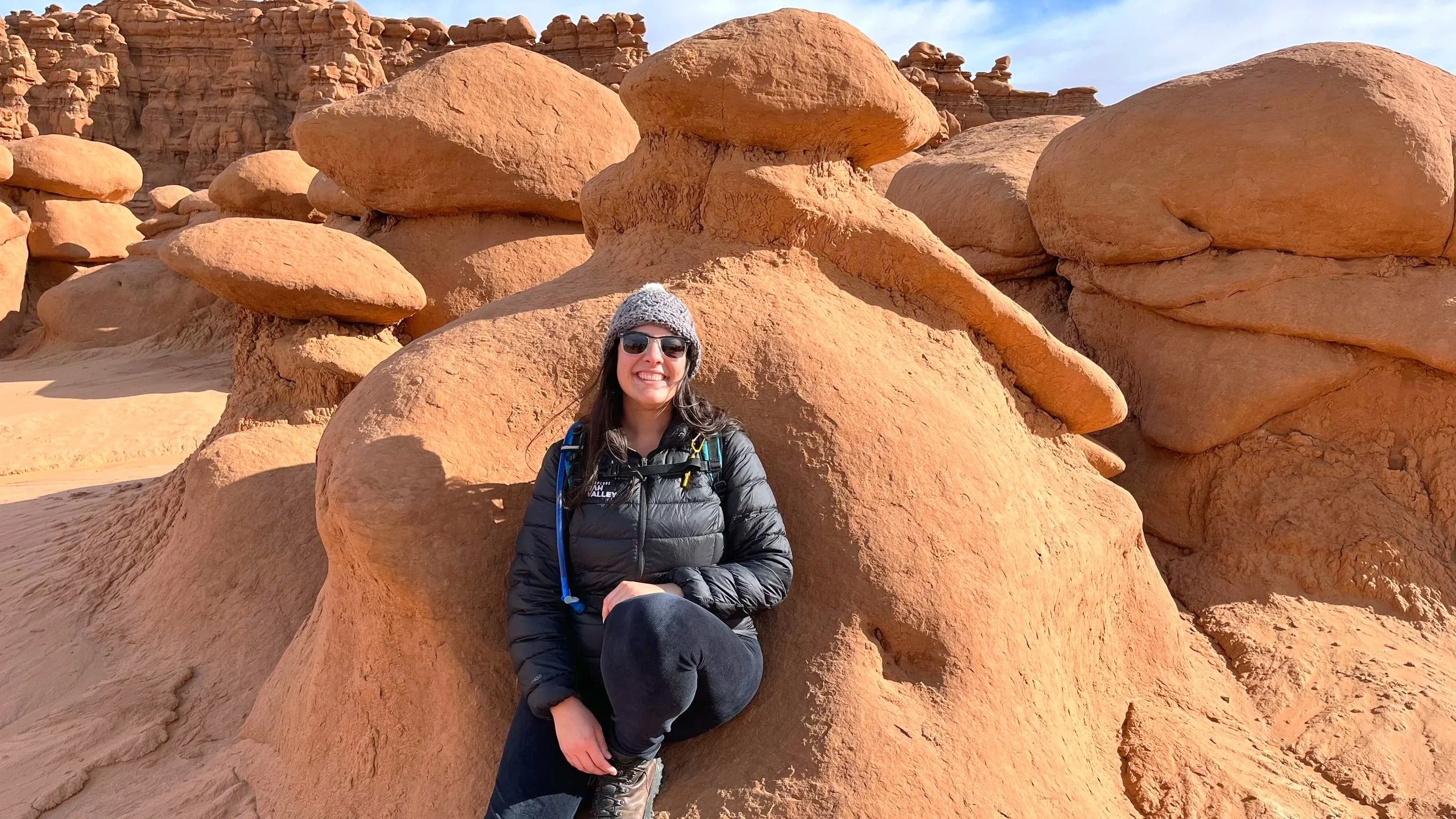 Hiking as a solo woman in Goblin Valley, posed against a hoodoo