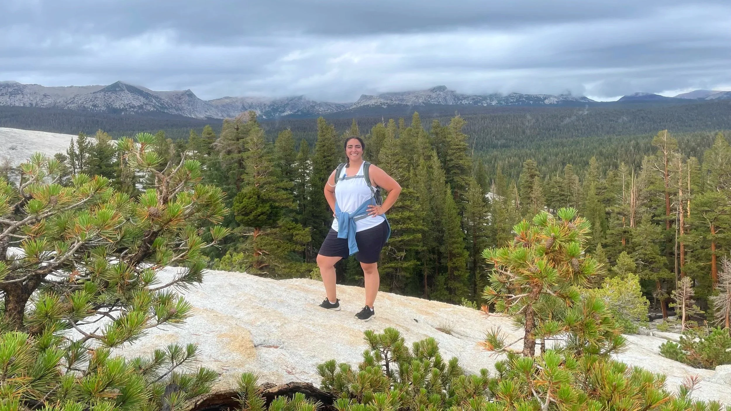 A woman poses on a granite dome while hiking in Yosemite.