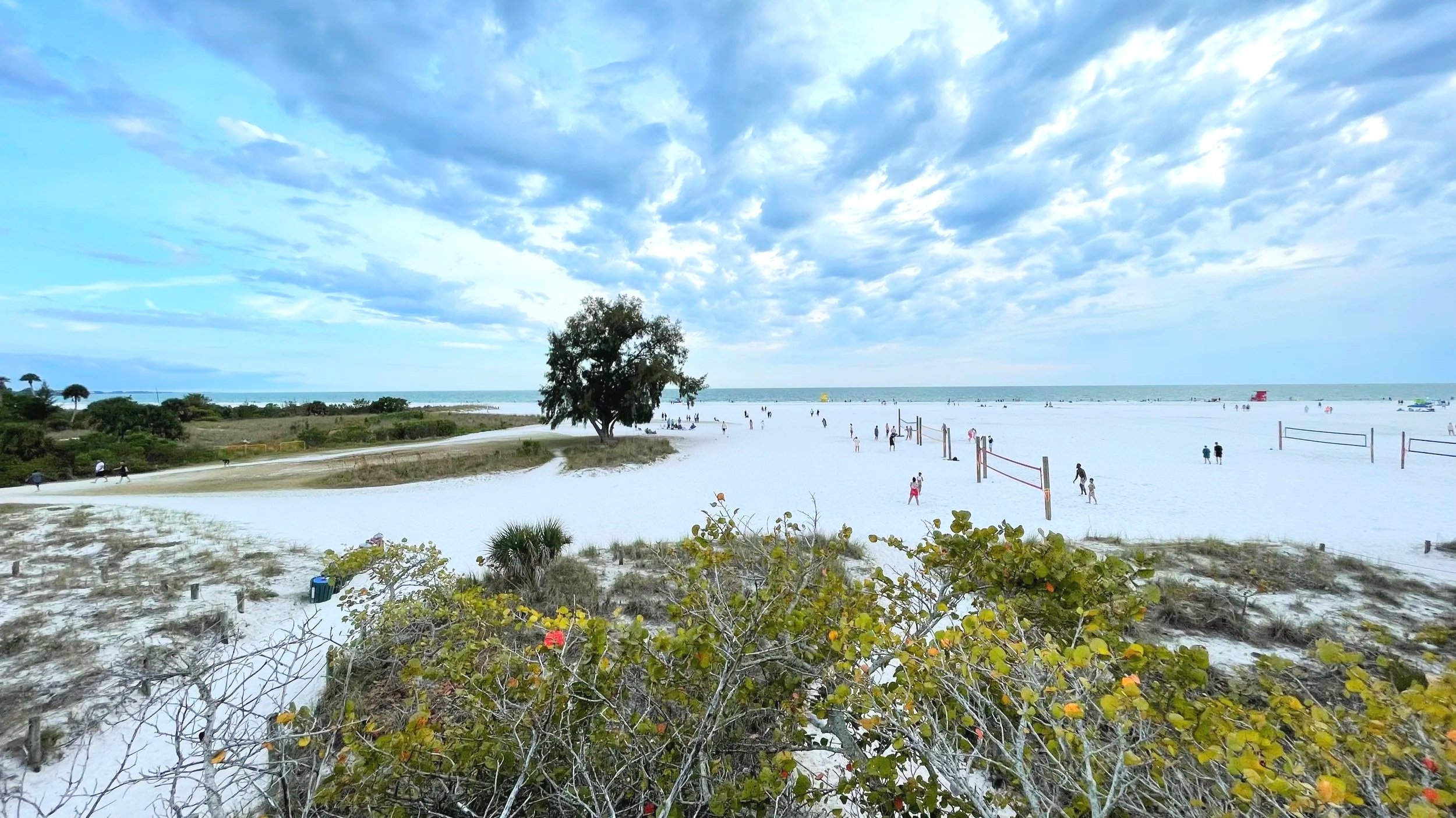 A white sand beach in Florida shows people playing volleyball.