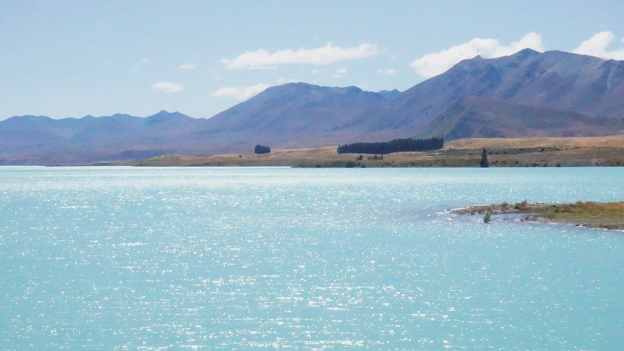 A strikingly blue Tekapo Lake in New Zealand's South Island glistens in the sun.