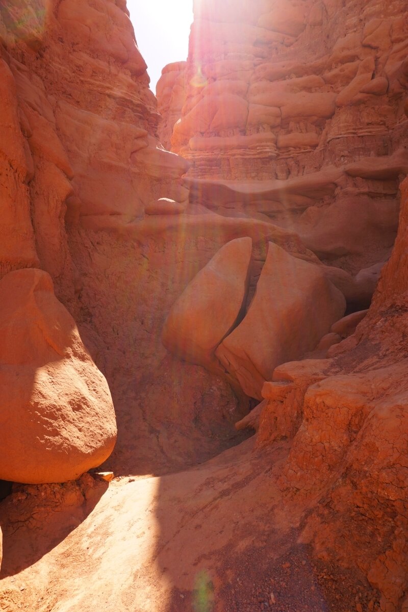 Sun shining through red rocks in Utah's Goblin Valley State Park valley of goblins hiking trail