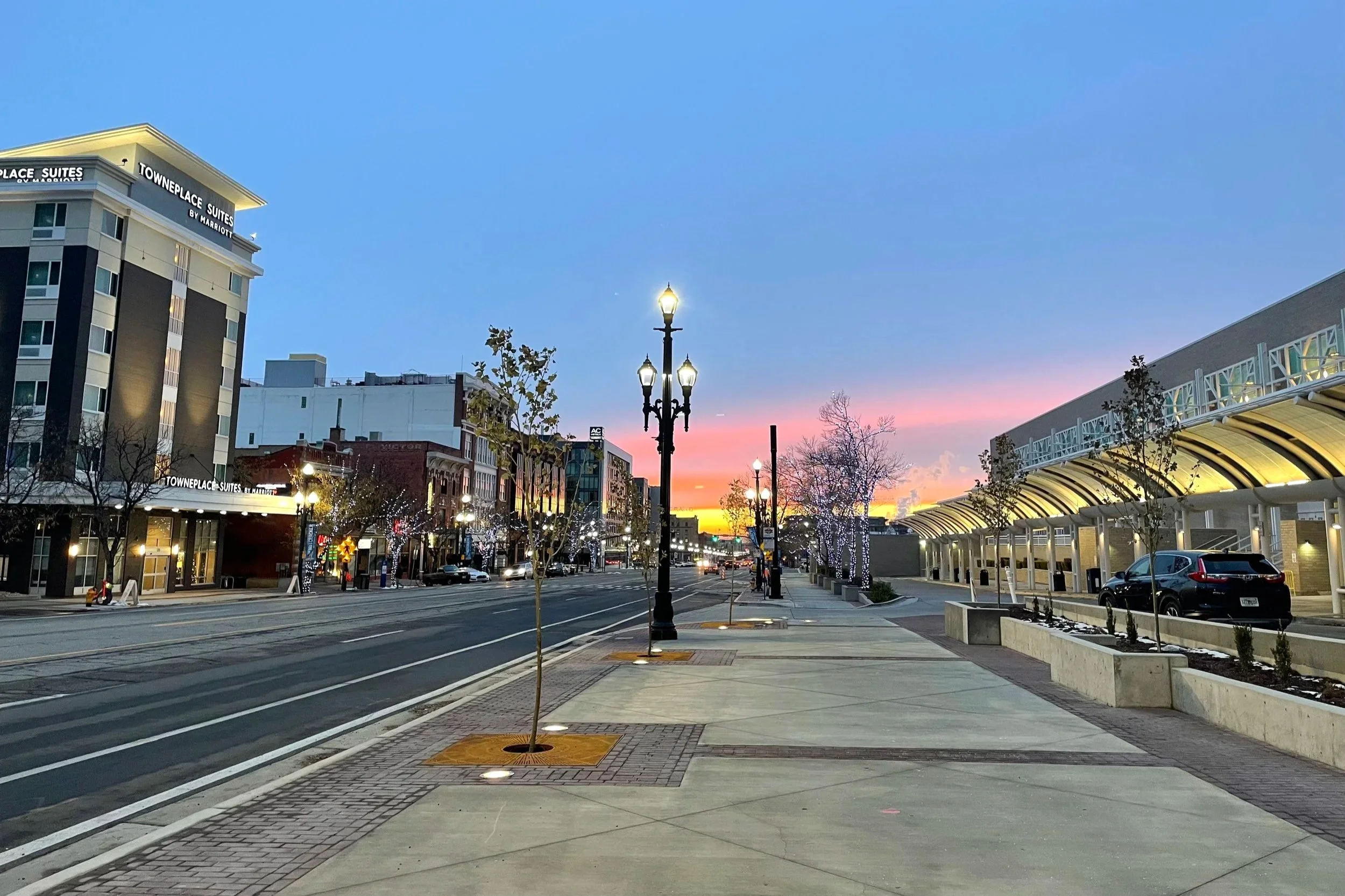 Downtown Salt Lake City with tall buildings on one side of the street and the convention center on the other side;  a faint pink glow lines the sky.