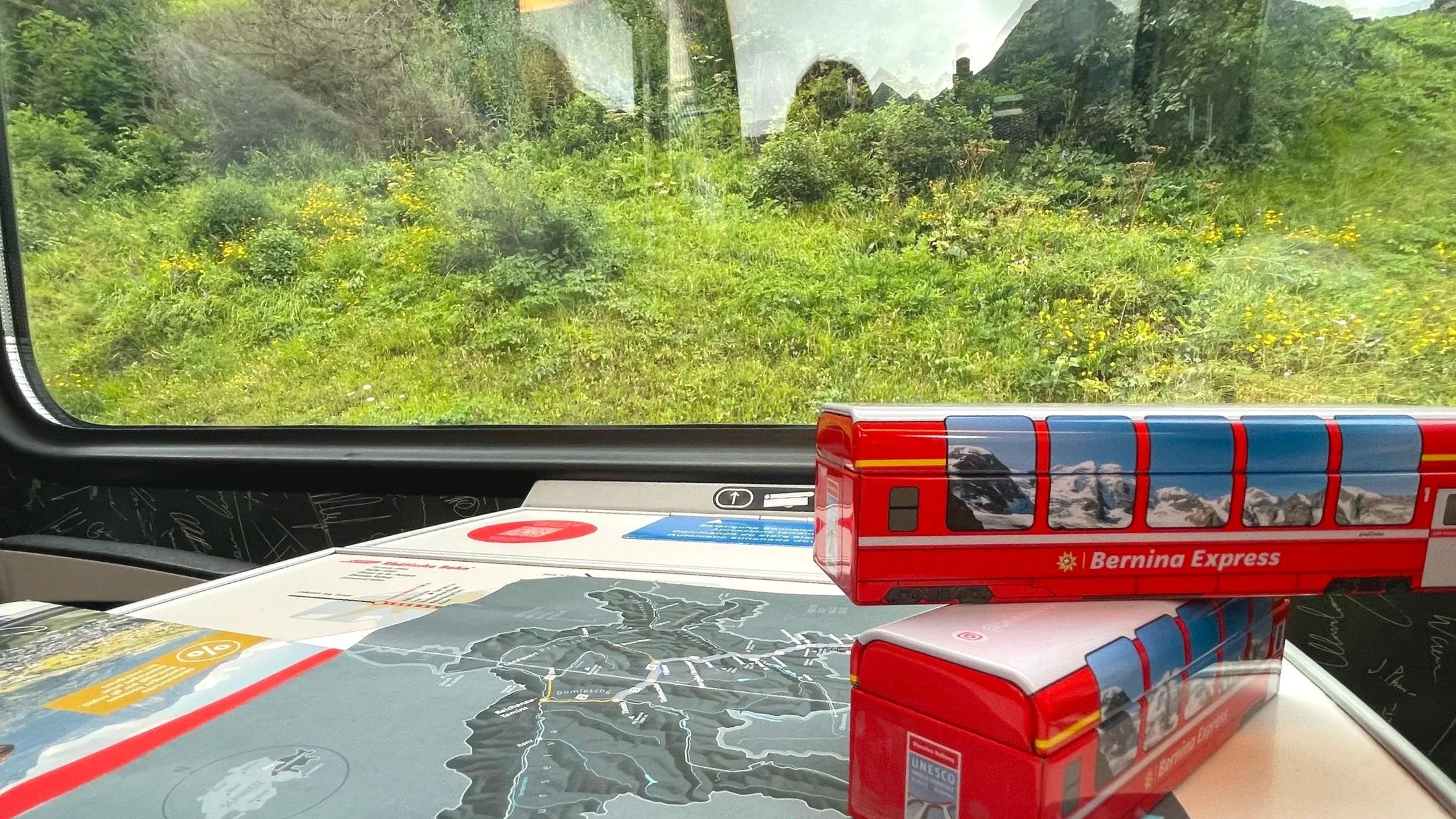 A peek out the window of the Bernina Express with a map and metal train on the table