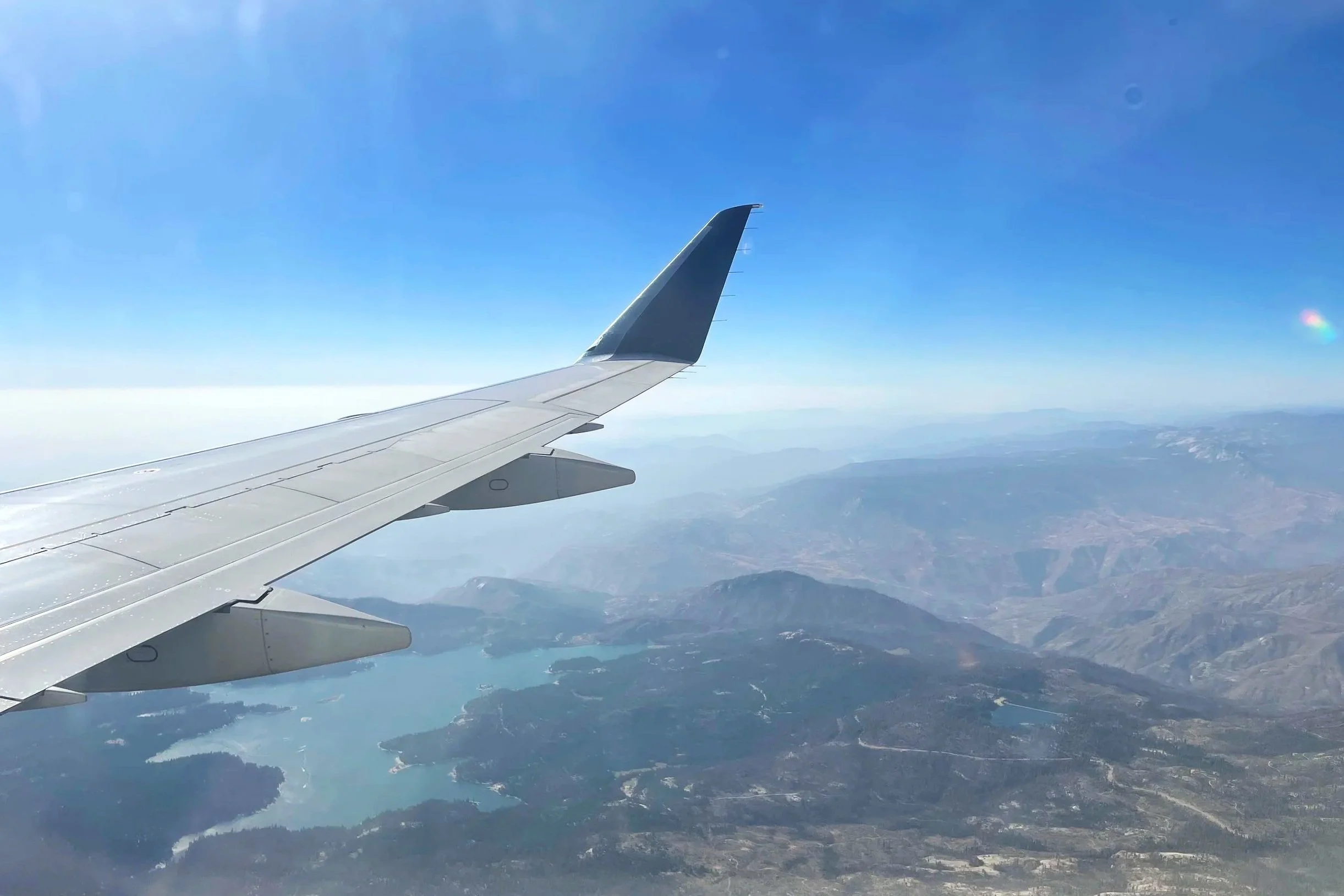 Airplane wing flying over mountains and a lake in the US.