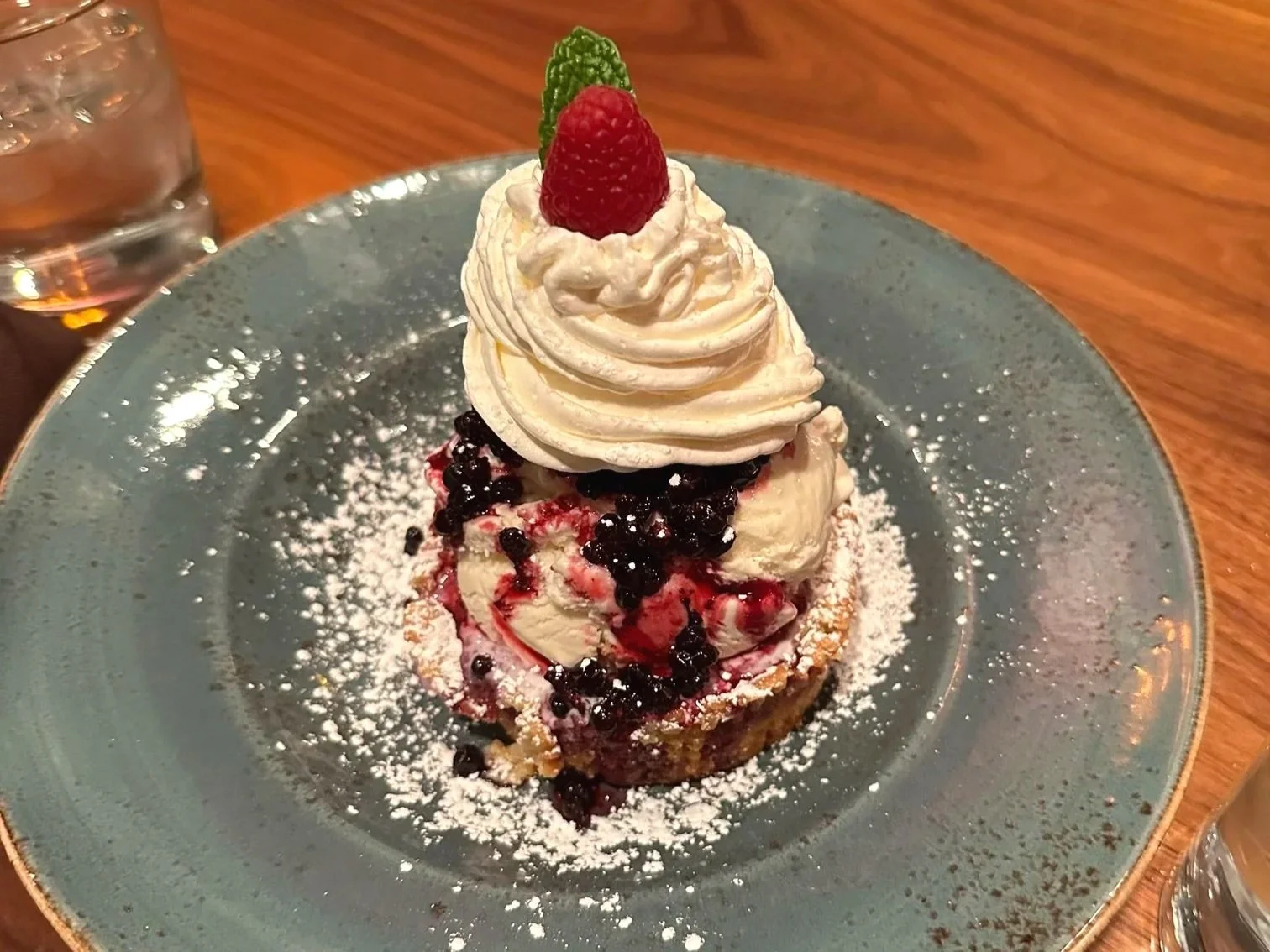 A delicious fruit tart piled high with berries, ice cream, whipped cream, and a raspberry on top.