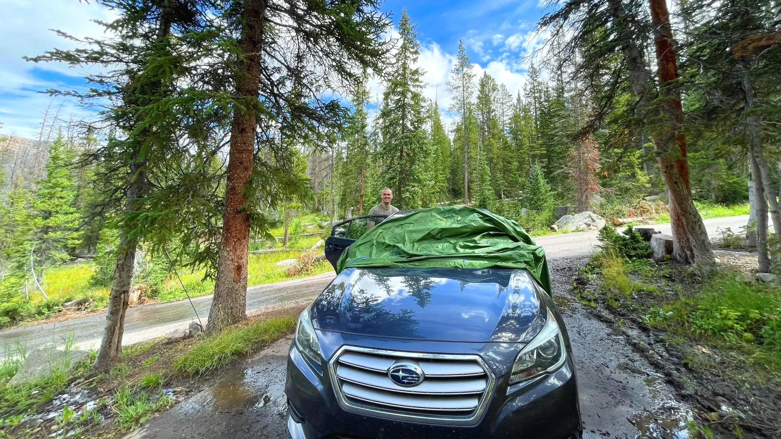 A car parked at a rainy campground with a man loading up the car.
