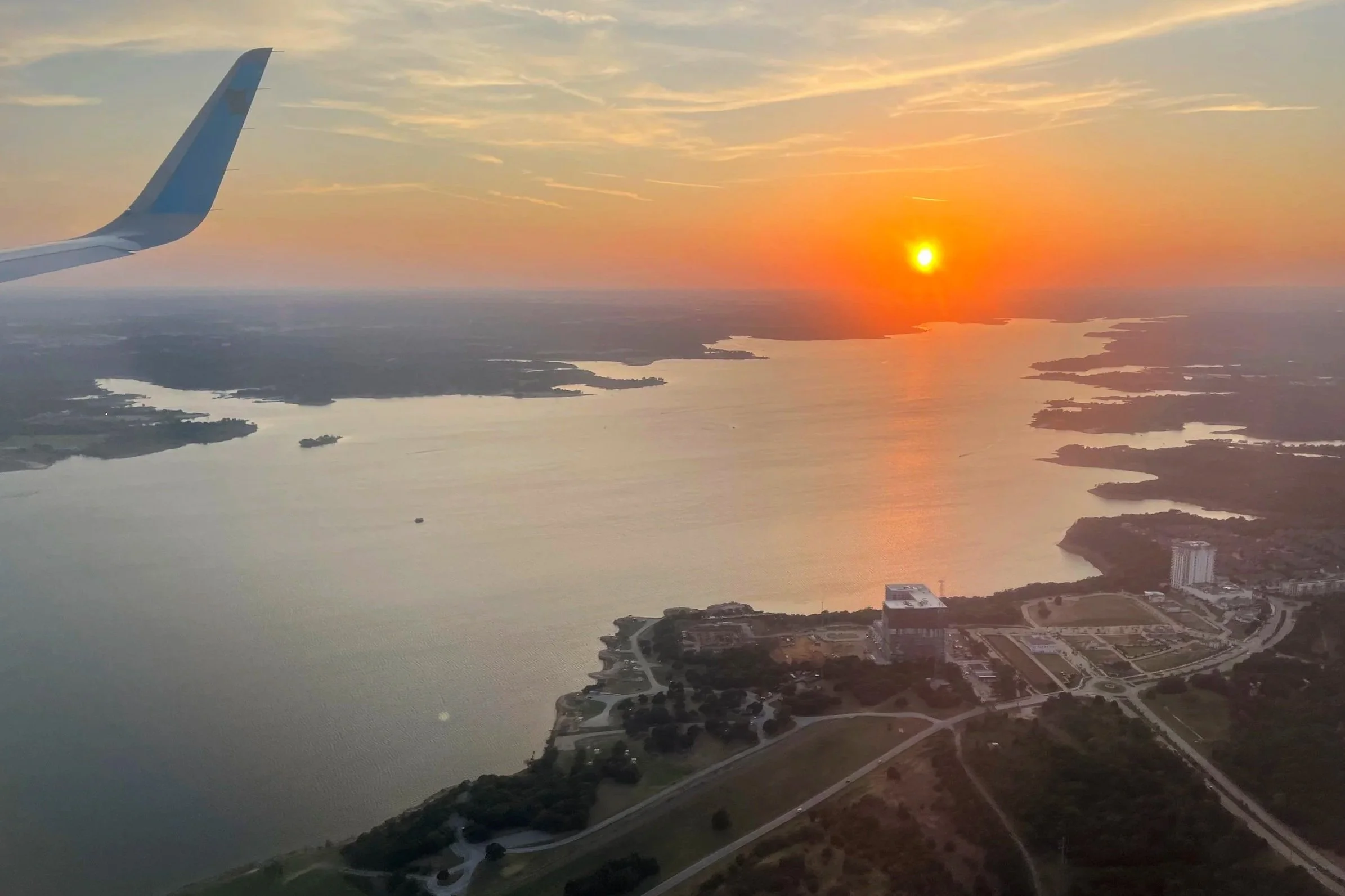 Airplane in the sky with sunset on the horizon shining on the water.