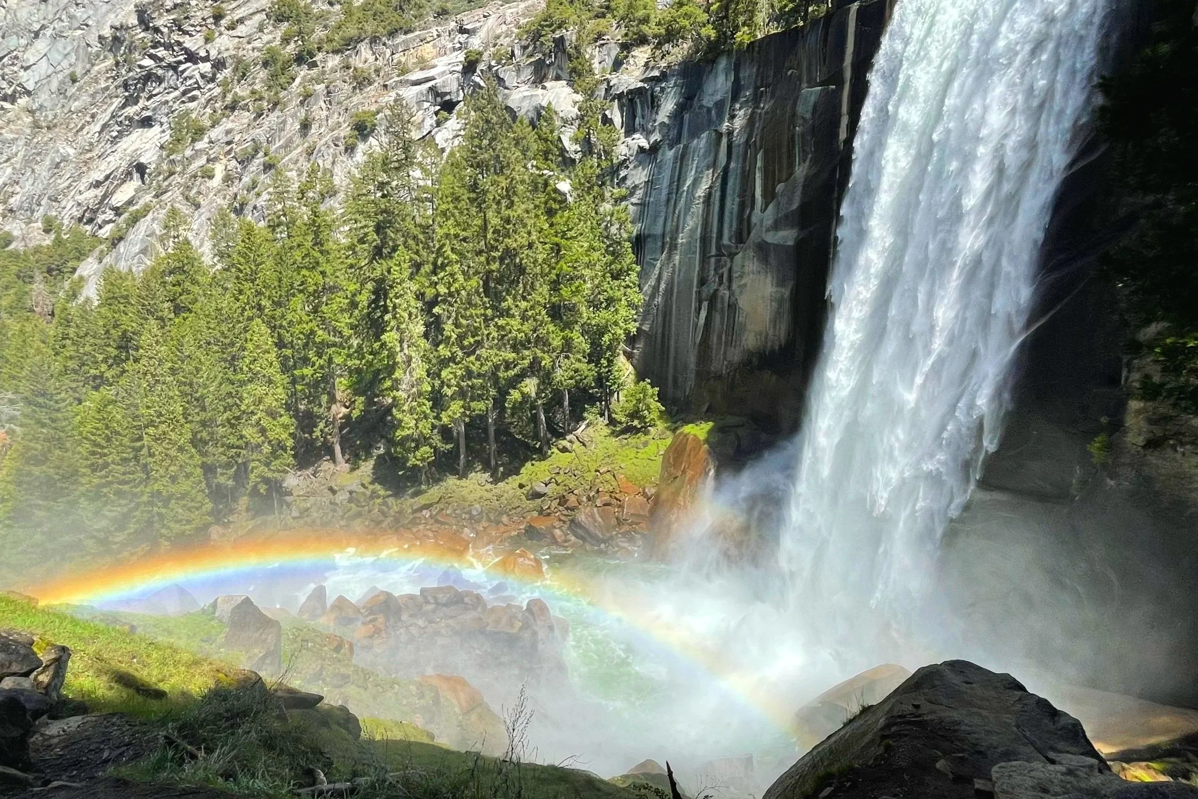 Vernal Fall in Yosemite flows forcefully into a river shining with a rainbow.