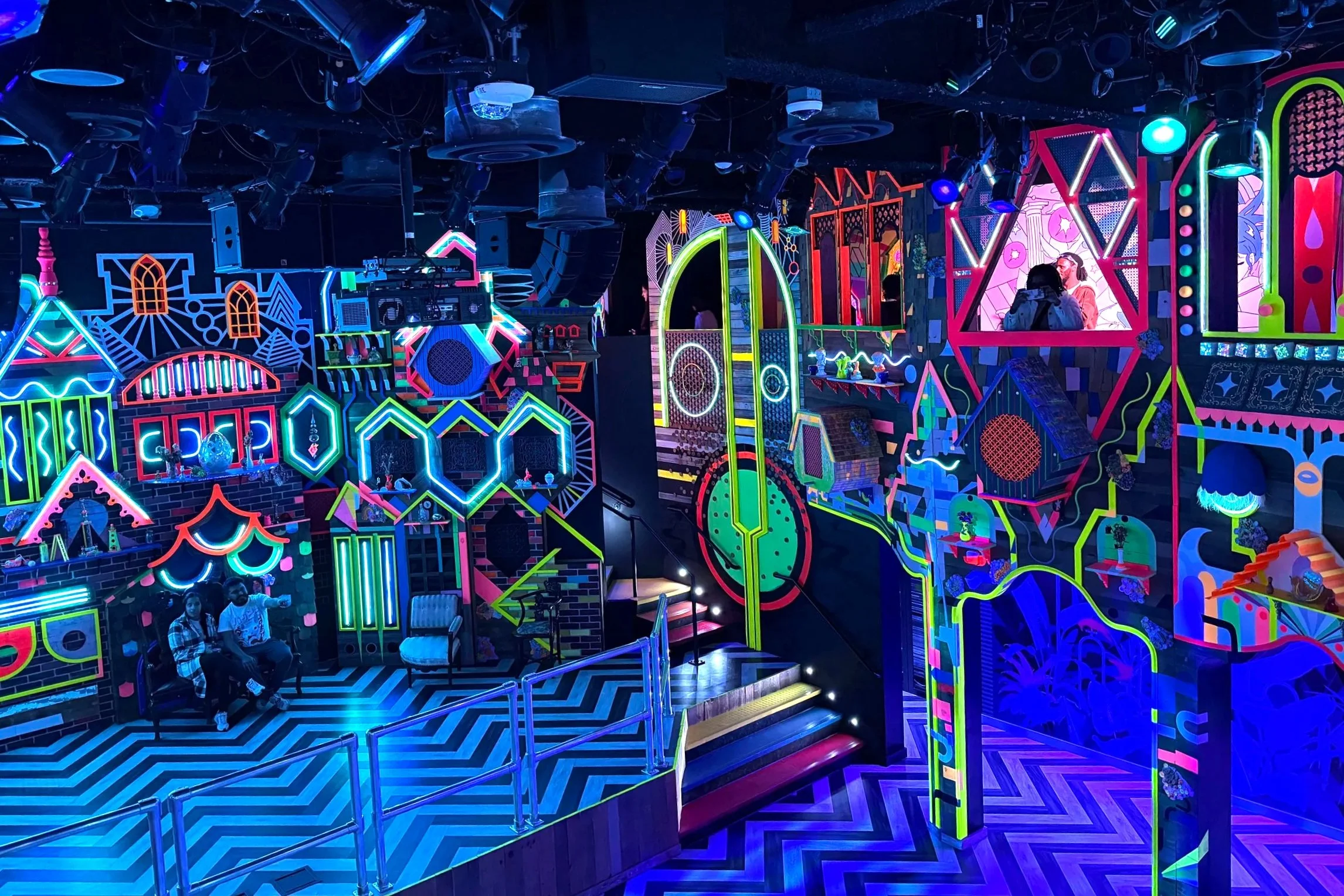 The Real Unreal at Meow Wolf, featuring a room with neon accents, busy patterns, and blue lights.