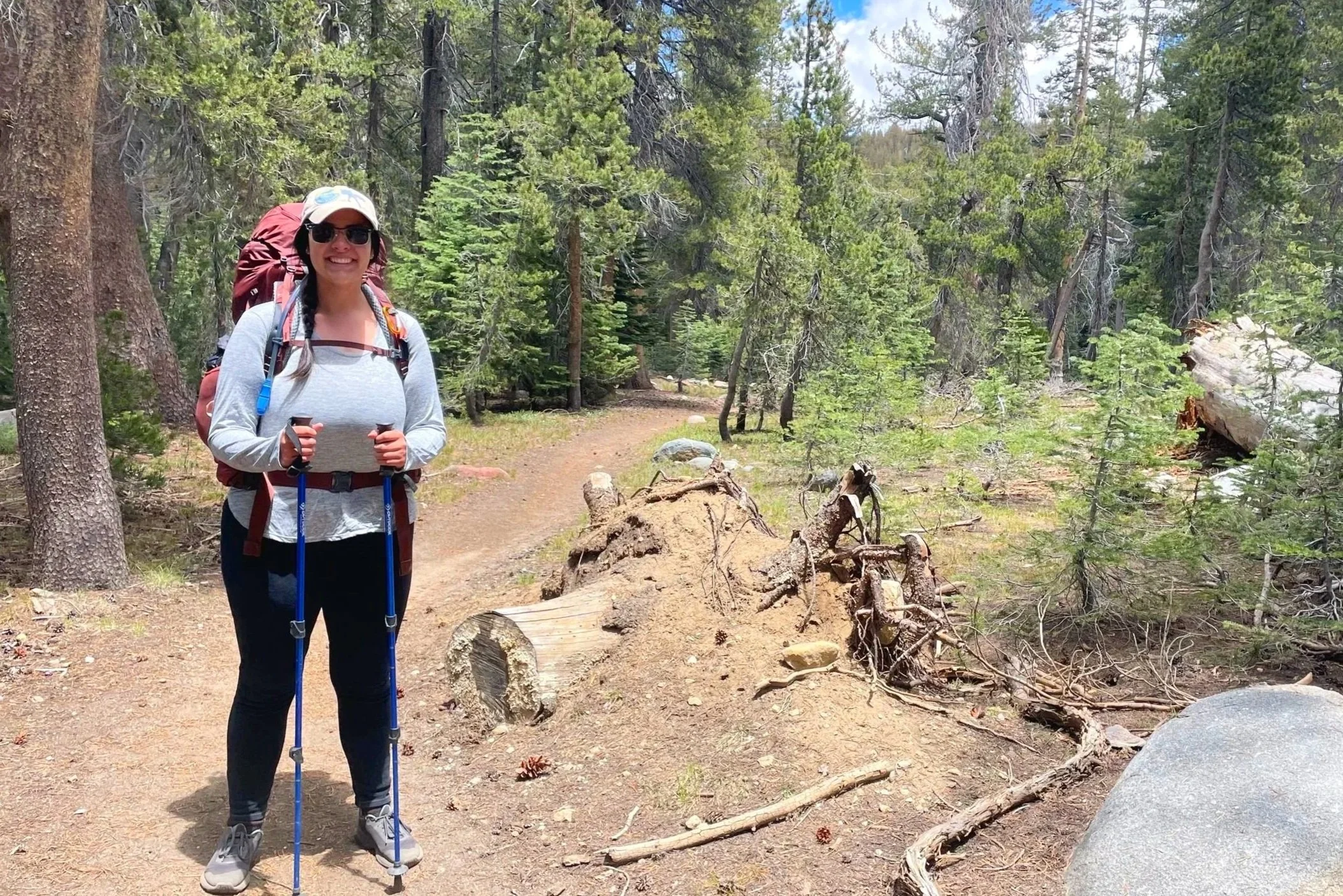A backpacker poses with a maroon pack on a forested trail.