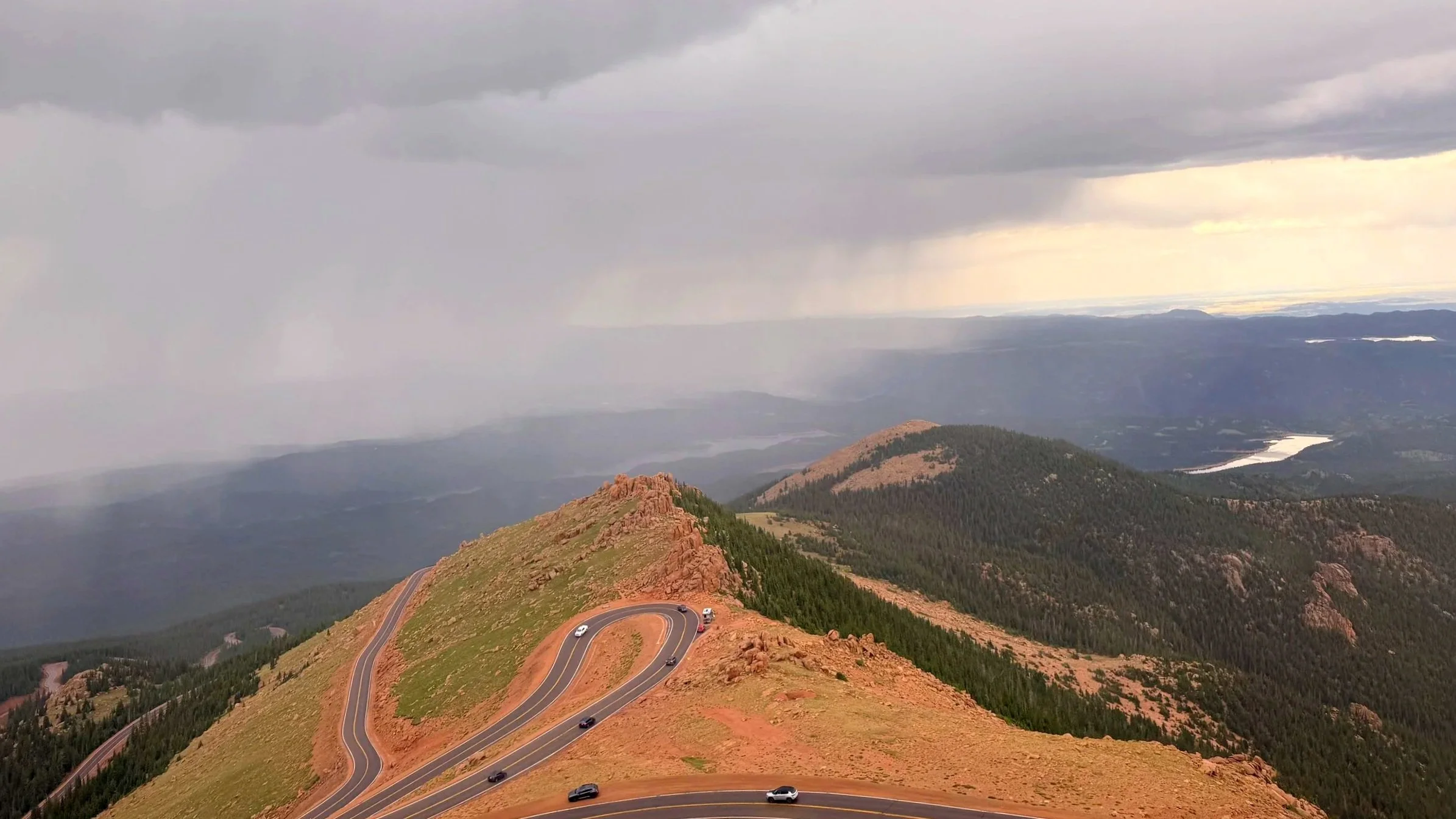 A windy mountain road descends into a rainstorm.