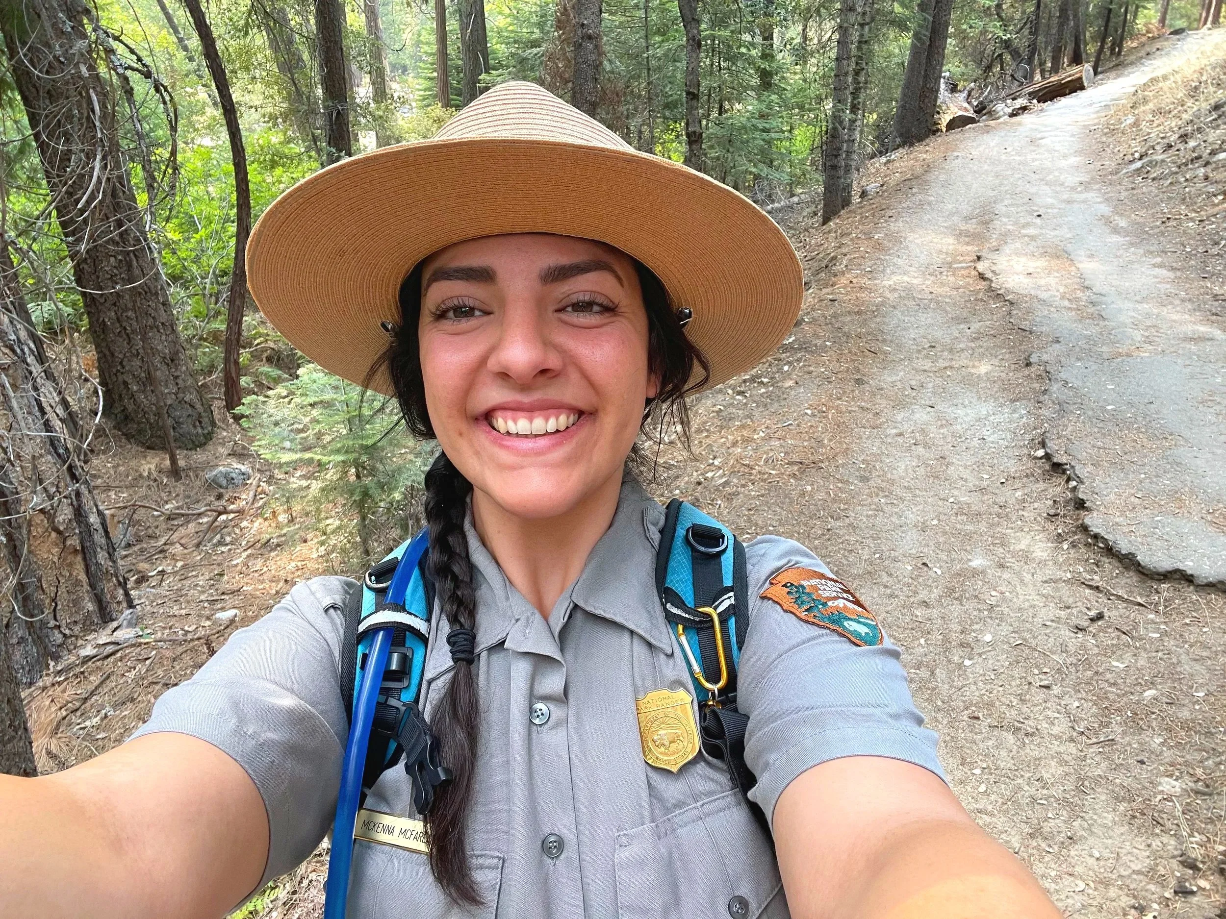 A park ranger dressed in uniform smiles on a trail in Yosemite.