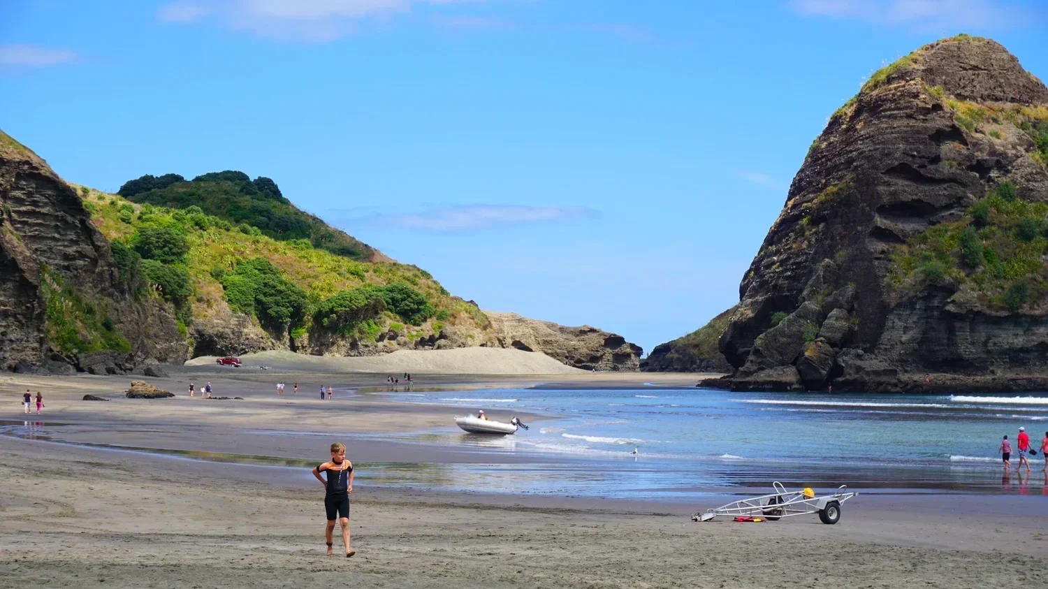 Piha Beach in New Zealand has people dotting the shore between green hills and grey cliffs
