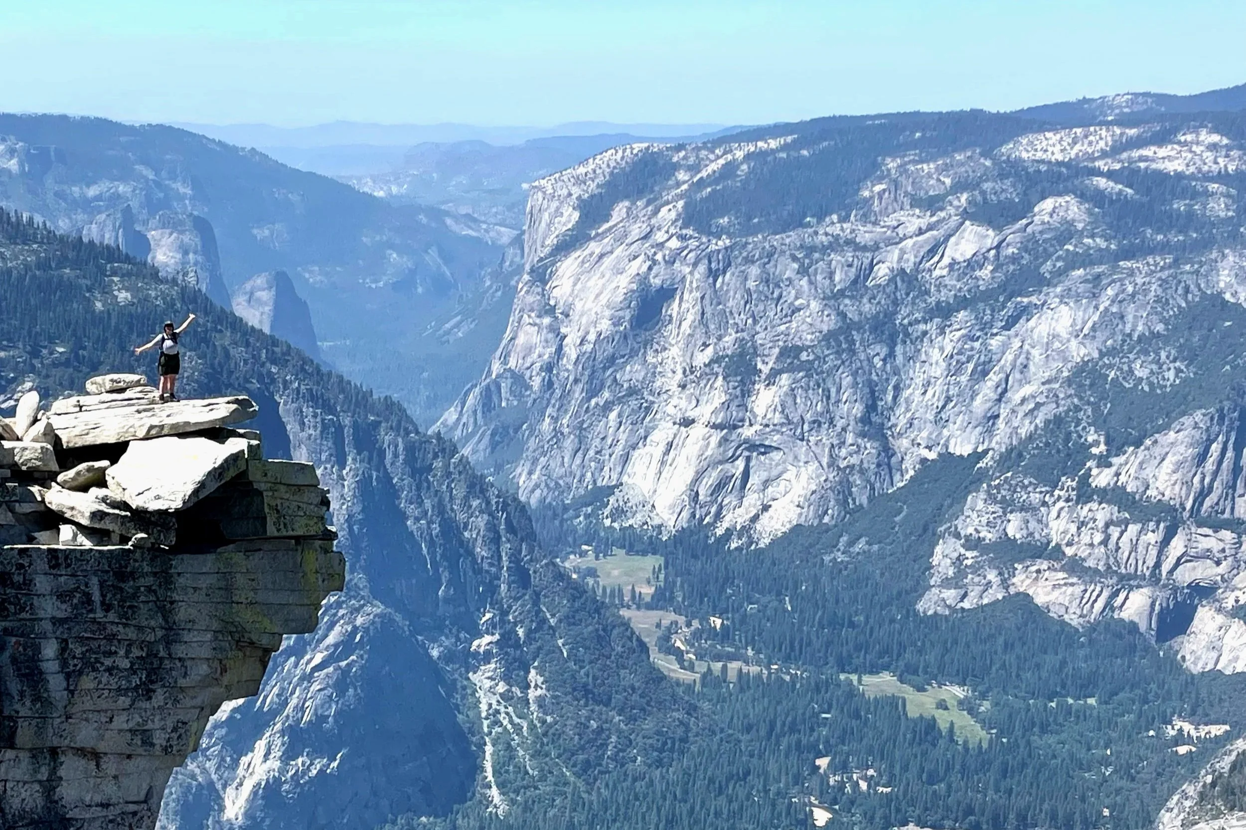 A park ranger poses on top of Half Dome, with expansive views of Yosemite Valley below.