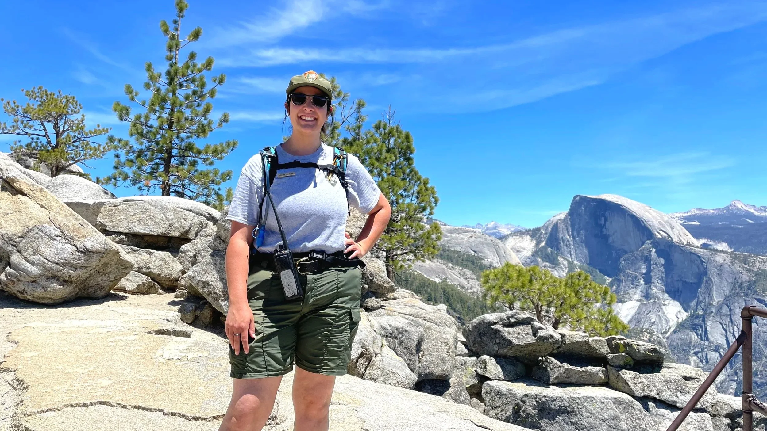 A park ranger in hiking gear poses with a view of Half Dome in the background.