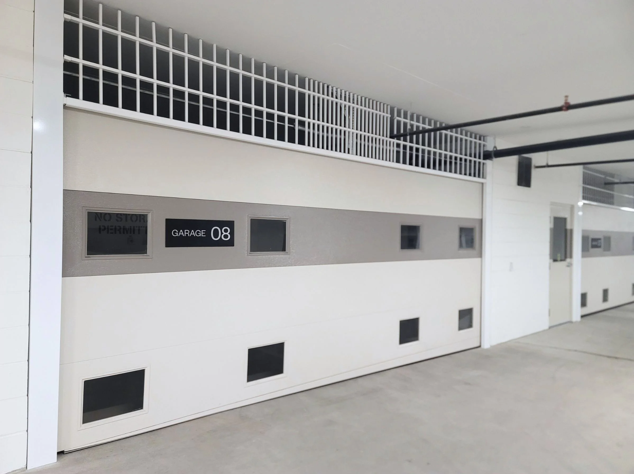 Indoor parking garage with white garage door labeled 'Garage 08' and 'No Stopping Permit' sign nearby.