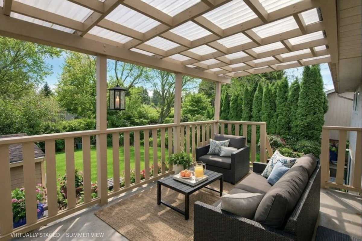 Covered outdoor balcony with seating area, sofa and armchair, coffee table with drinks and snacks, hanging lantern, overlooking a lush green yard with trees and shrubs.