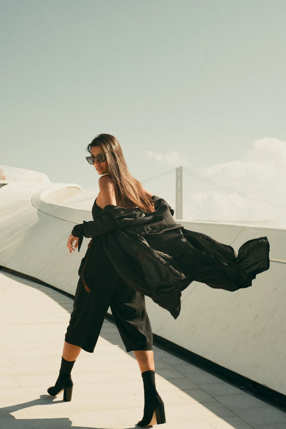 Editorial — mulher com casaco comprido na ponte, vento e movimento