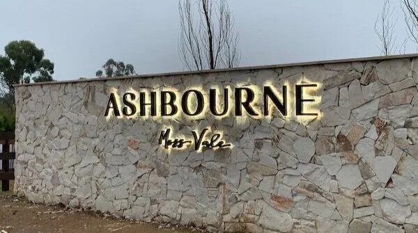 Halo-lit Ashbourne lettering above “Moss Vale” on a stone entrance wall.