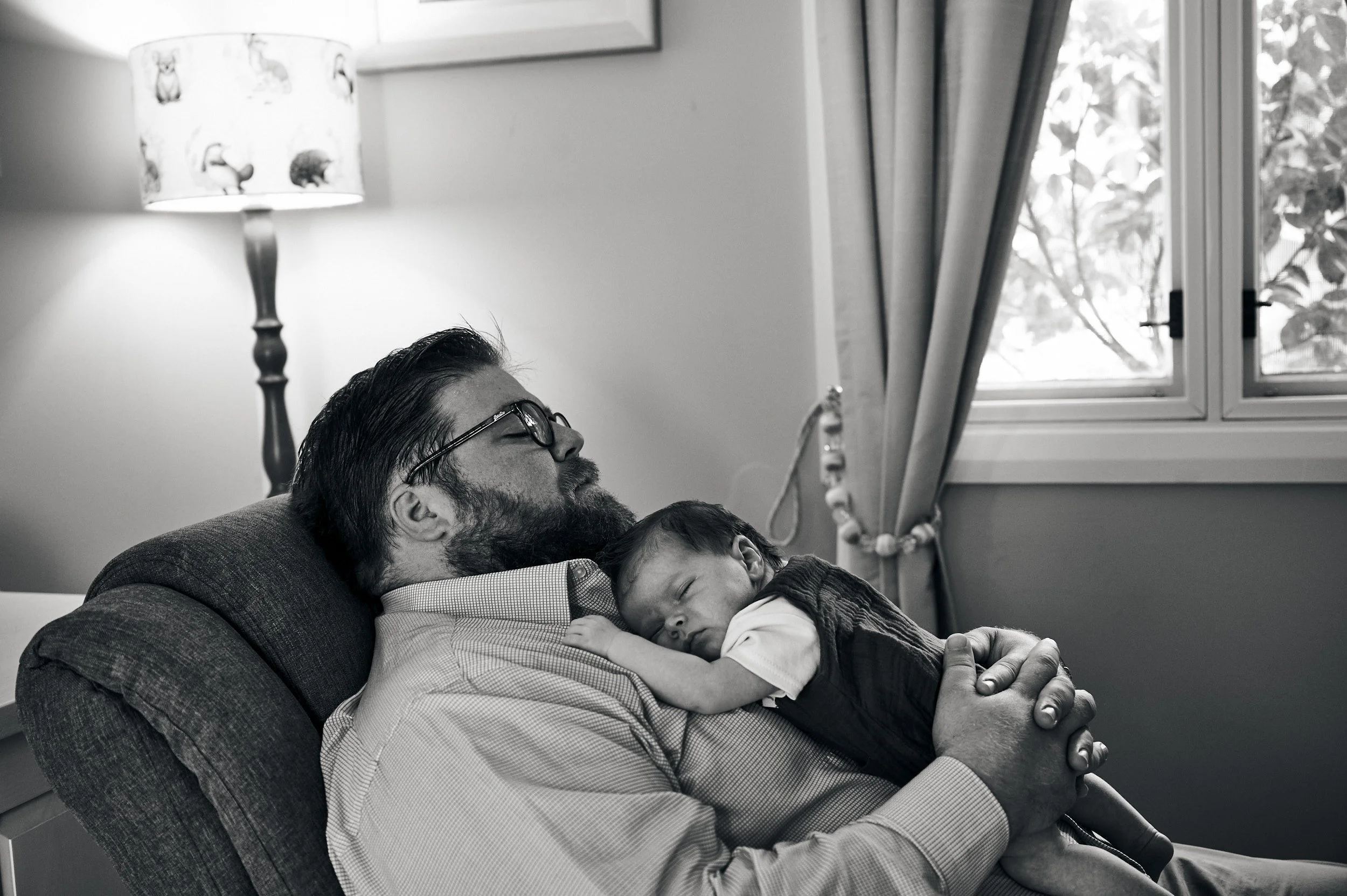 a dad snoozes in the comfort of his home while his baby rests on his chest