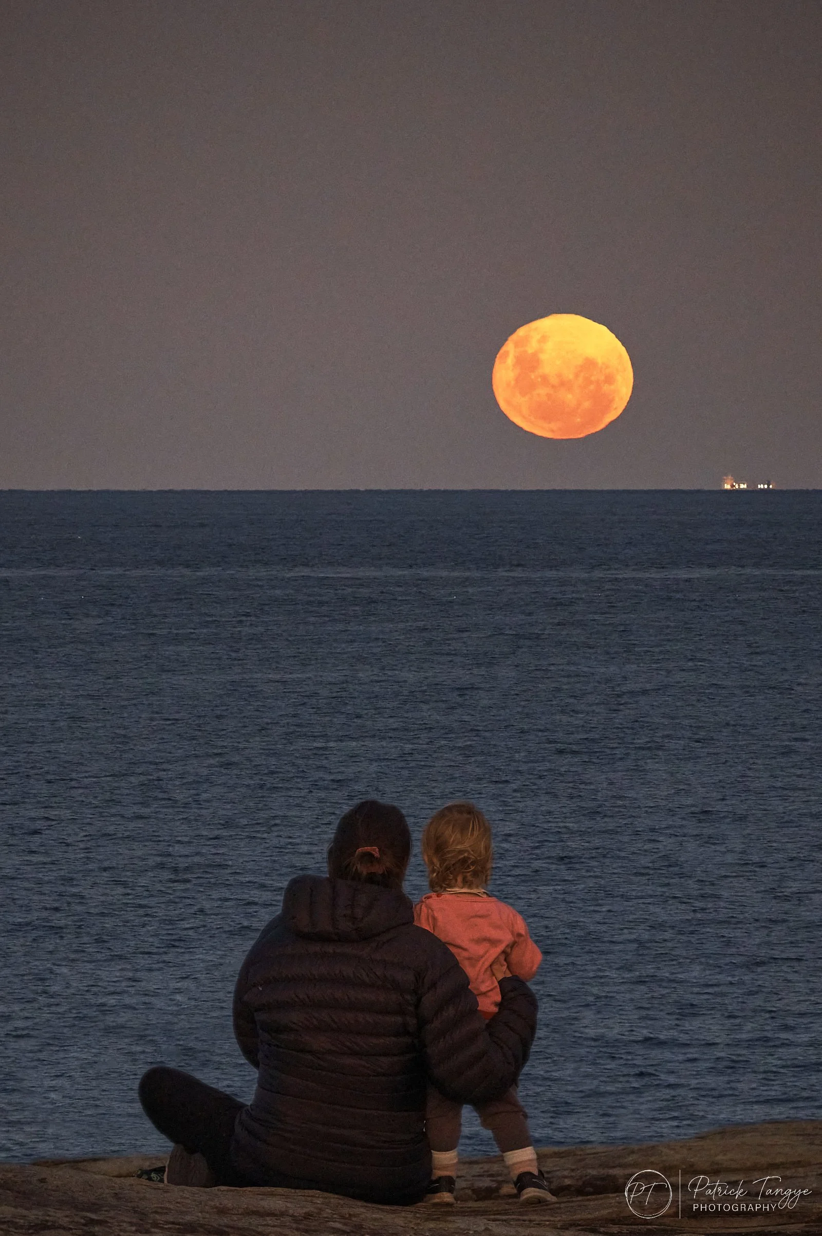 a mother and child sit on the cliffs at Coogee watching the full moon rising