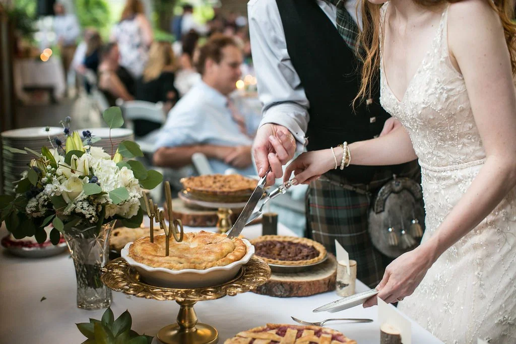 A bride and groom cutting a wedding cake at their reception with guests in the background.