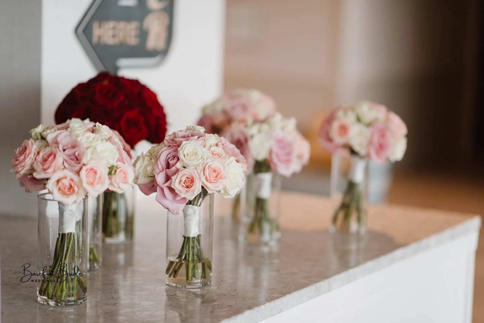Multiple glass vases filled with pink and white roses arranged on a marble surface.