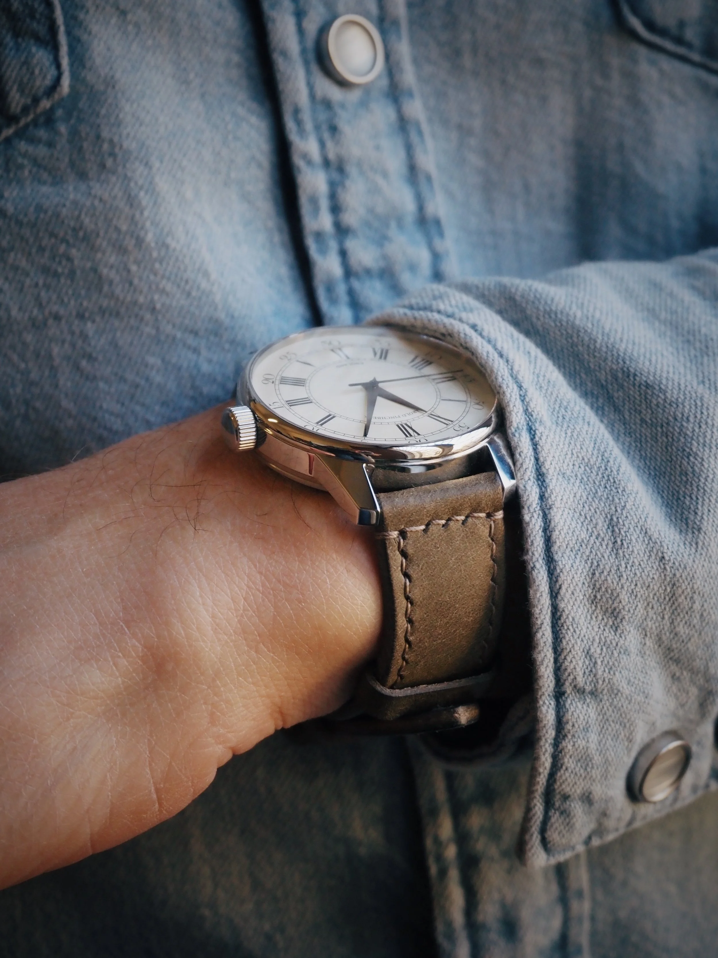 A person wearing a wristwatch with a leather strap and a white dial, showing the time as 4:14, with a denim shirt.