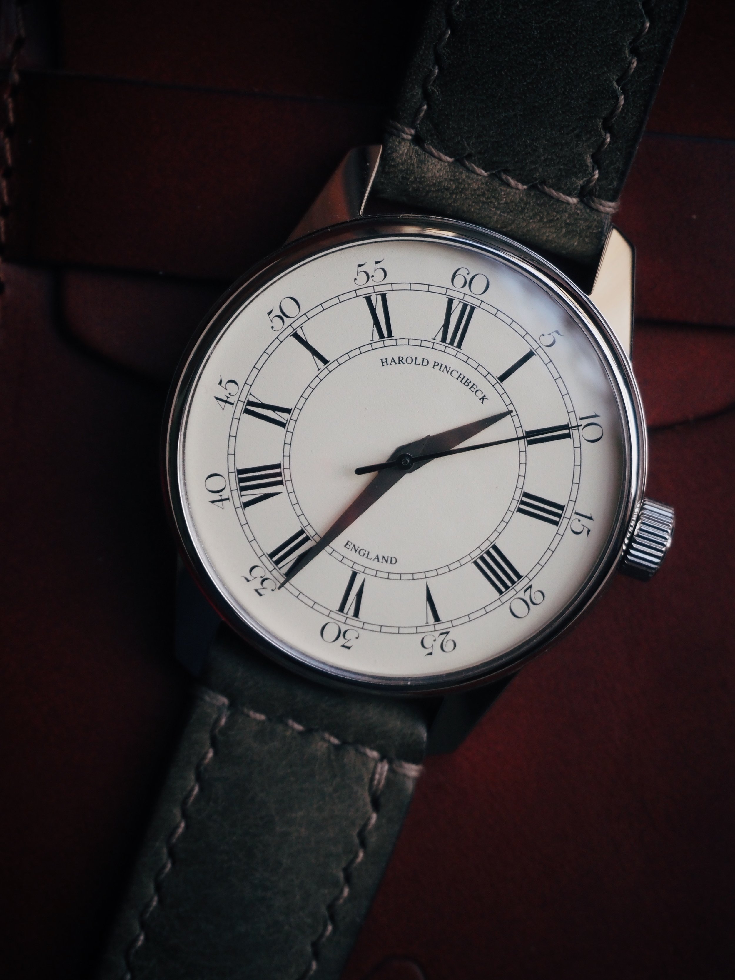 A wristwatch with a white dial, black Roman numerals, and a black leather strap.