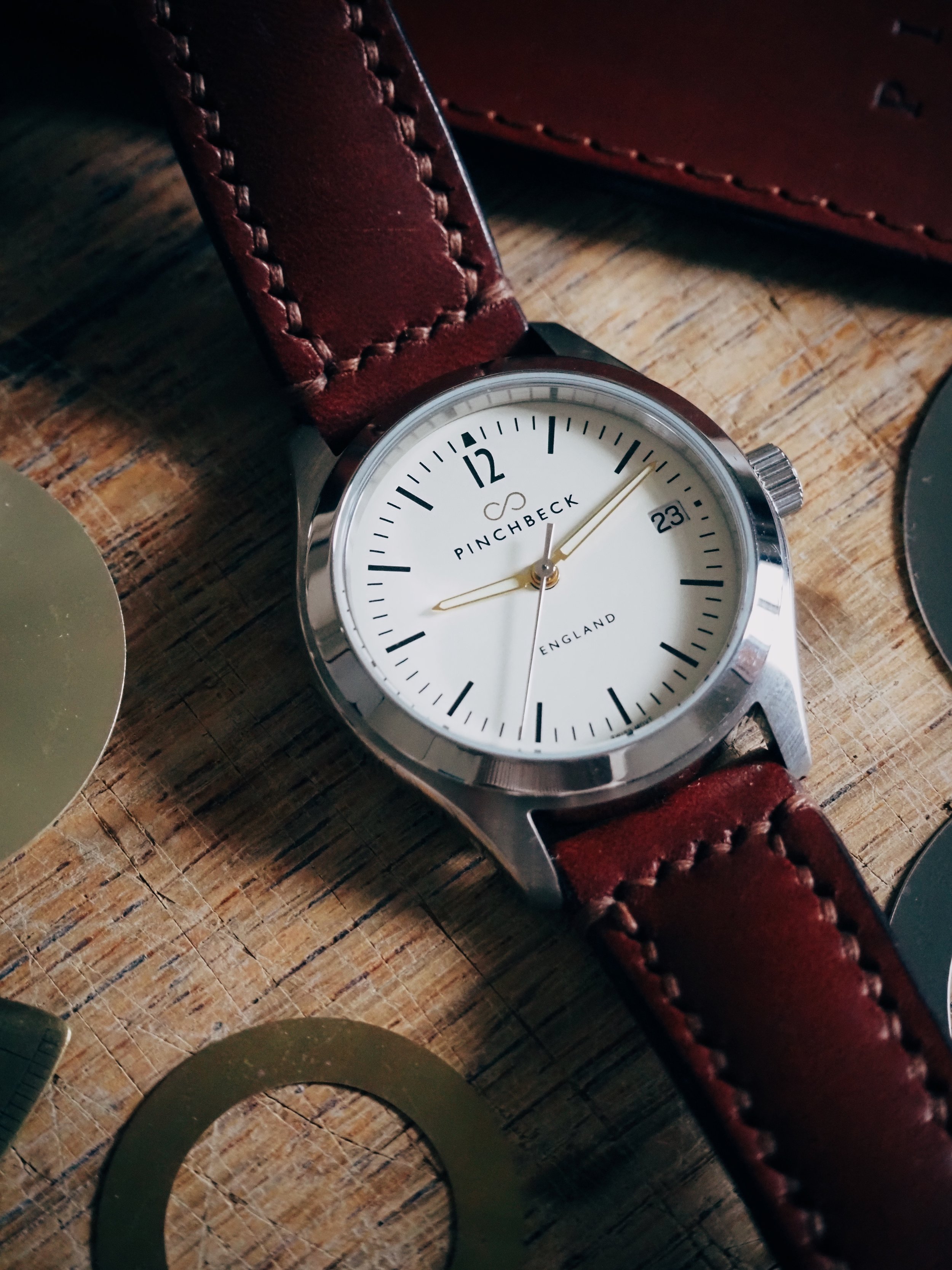 Luxury wristwatch with leather strap, white dial, and minimalist design, featuring "Pinchbeck" branding and date display.